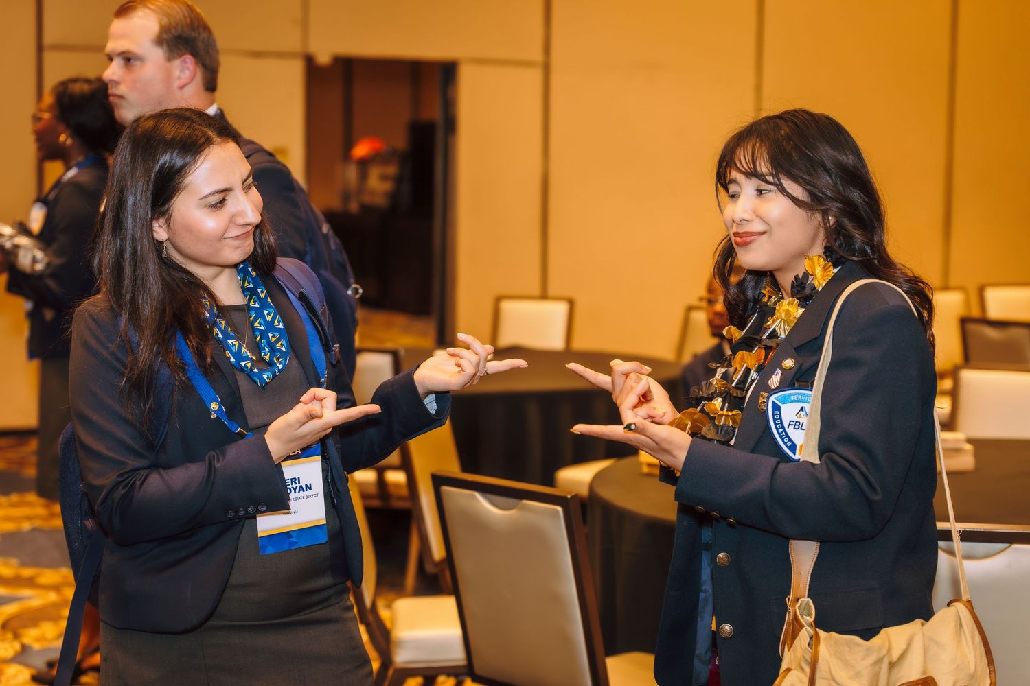 Two young women in business attire having an animated conversation at a professional networking event.