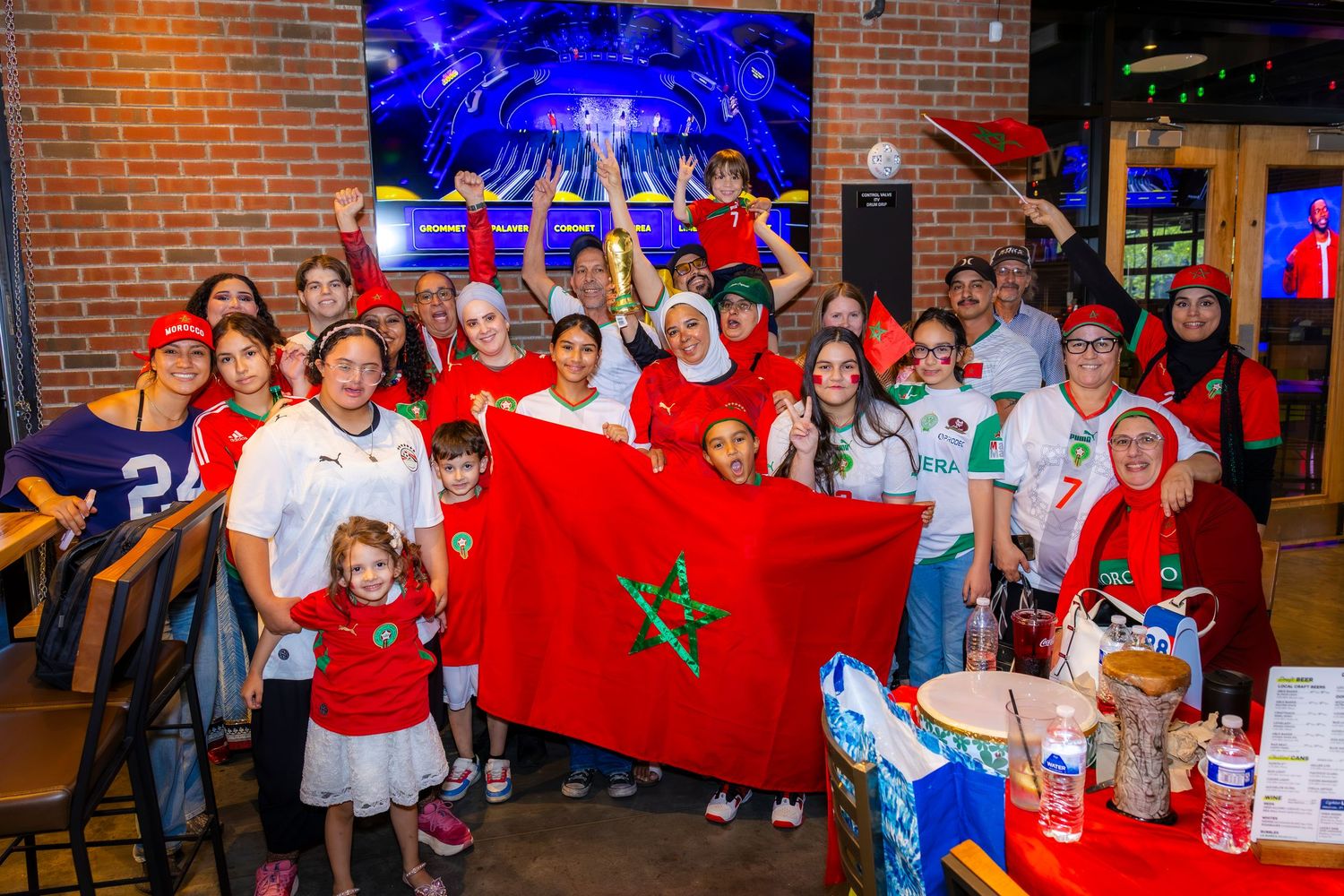 Group of Morocco soccer fans holding Moroccan flag at a sports bar watch party celebration.