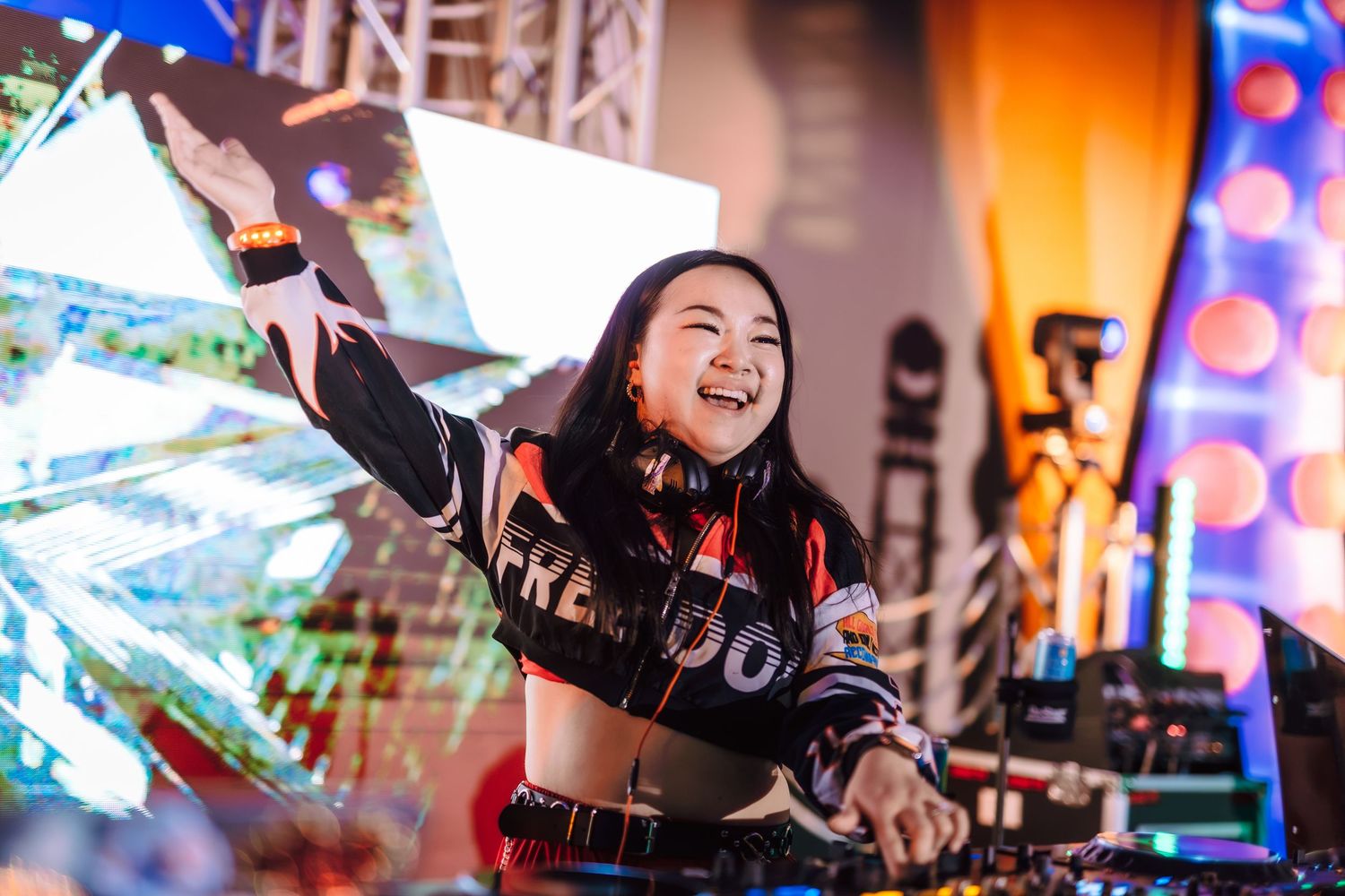 Female DJ performing energetically at a vibrant music festival stage.