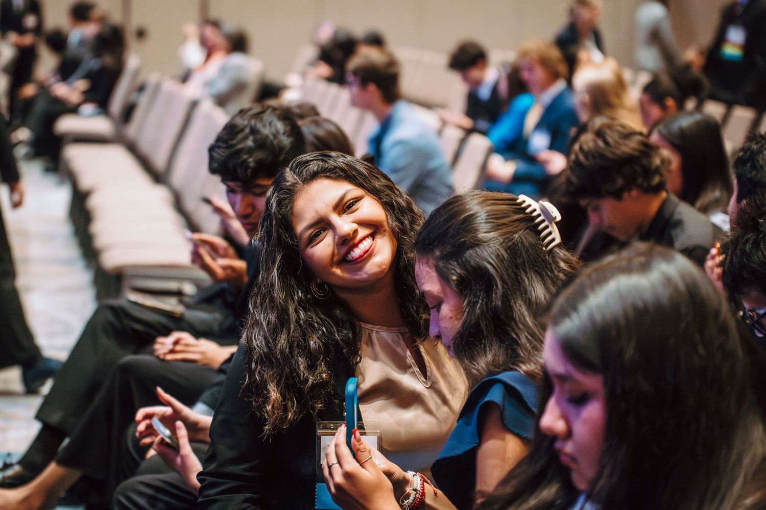 Smiling young woman with dark hair sitting among students at an academic conference.