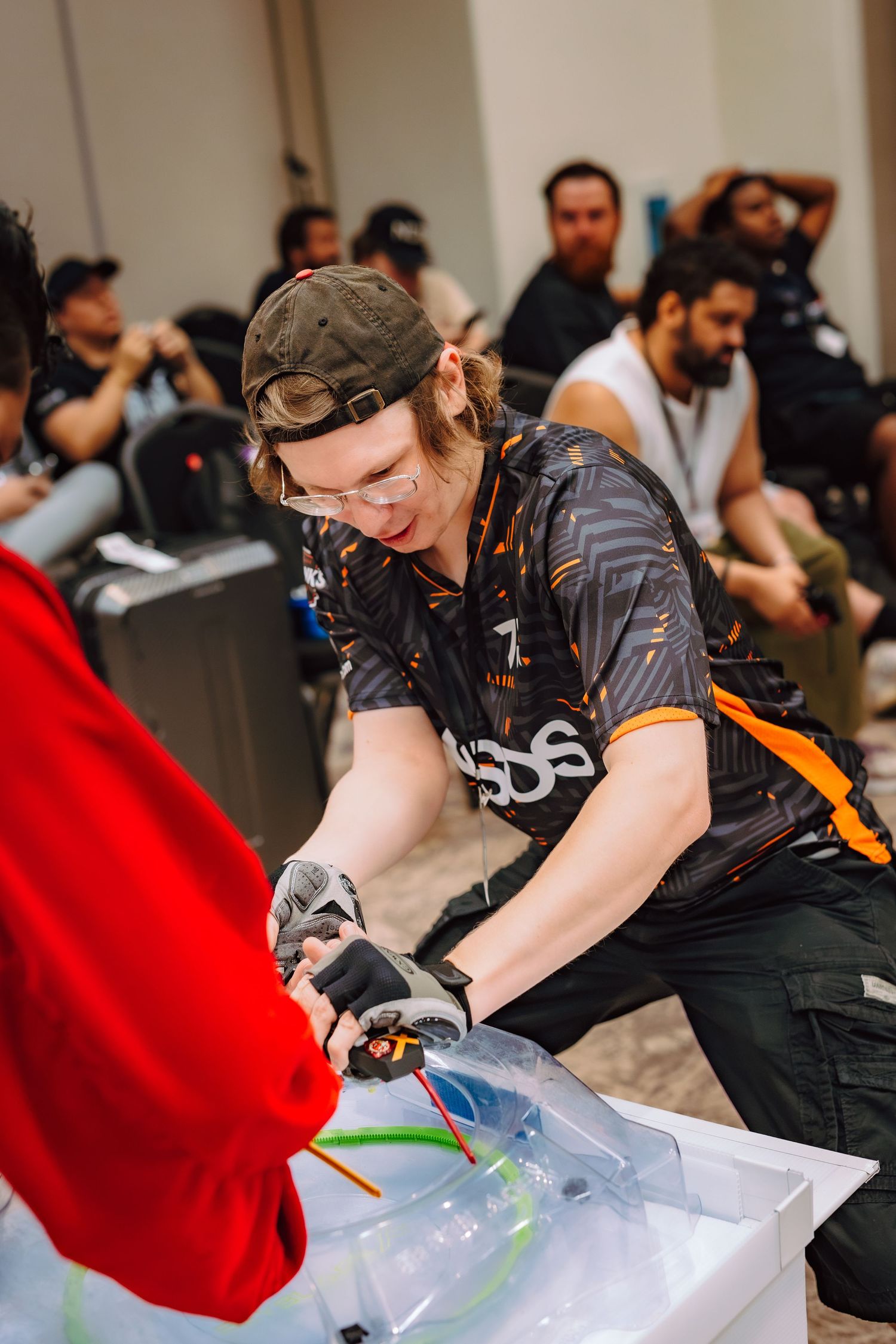Young man in gaming jersey and cap uses wire cutters on cables at an esports competition event.