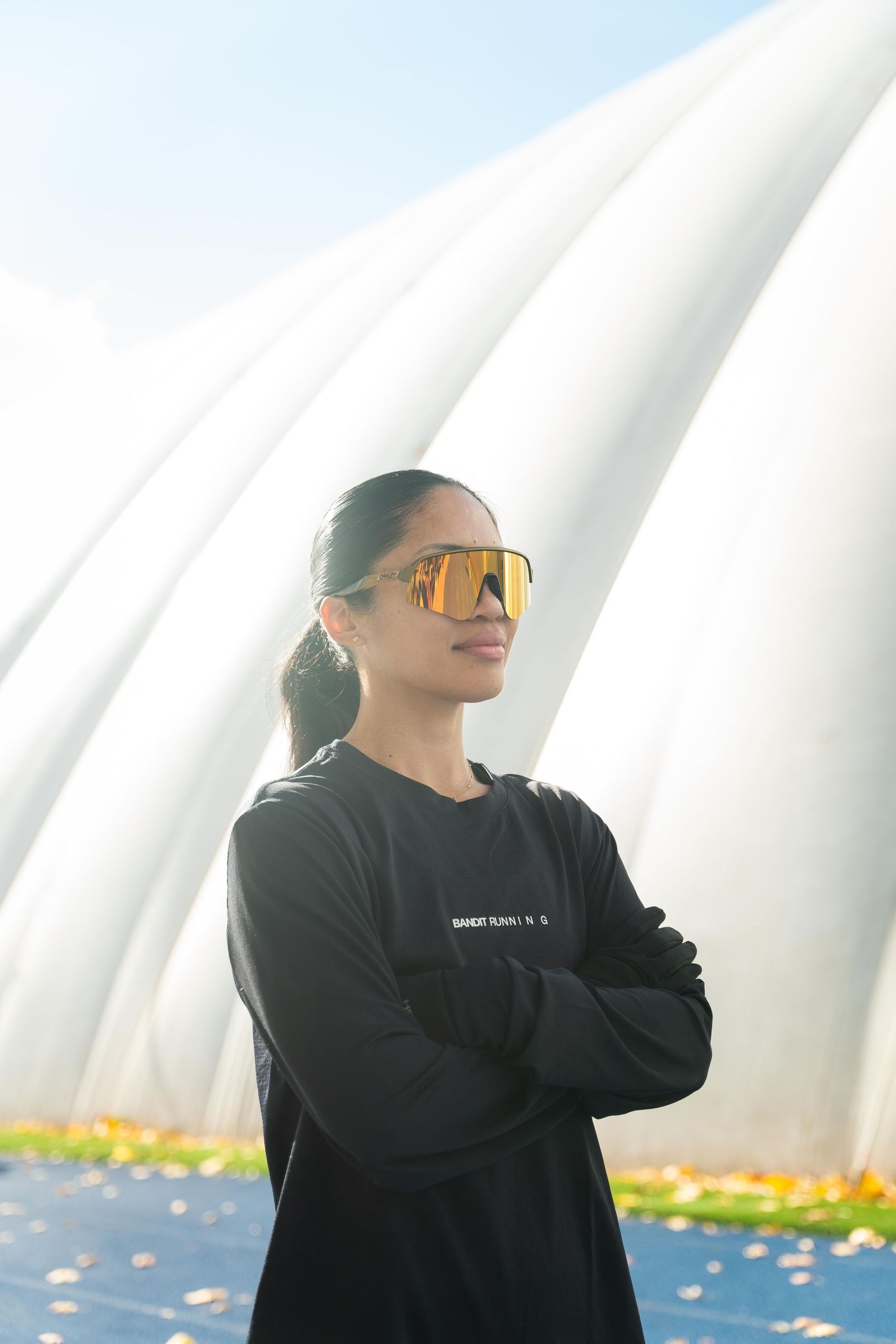A woman wearing sunglasses poses in front of a spacious white tent, highlighting a sunny outdoor event.