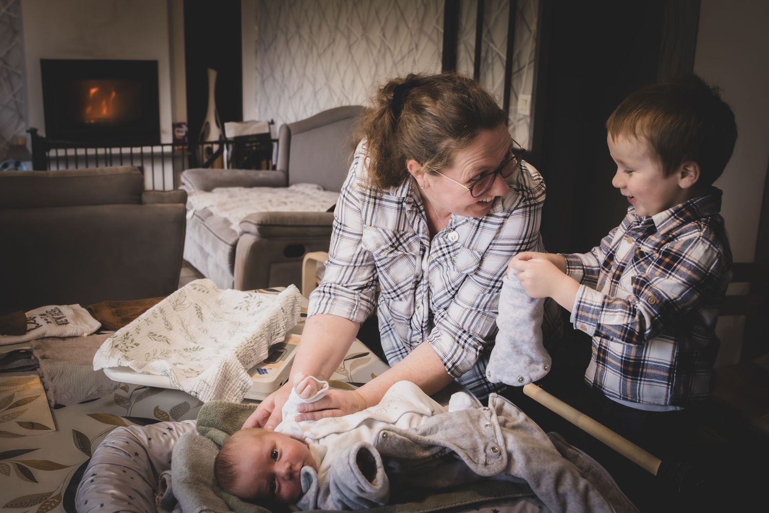 A parent and two children in matching plaid shirts share a playful moment together on a bed.