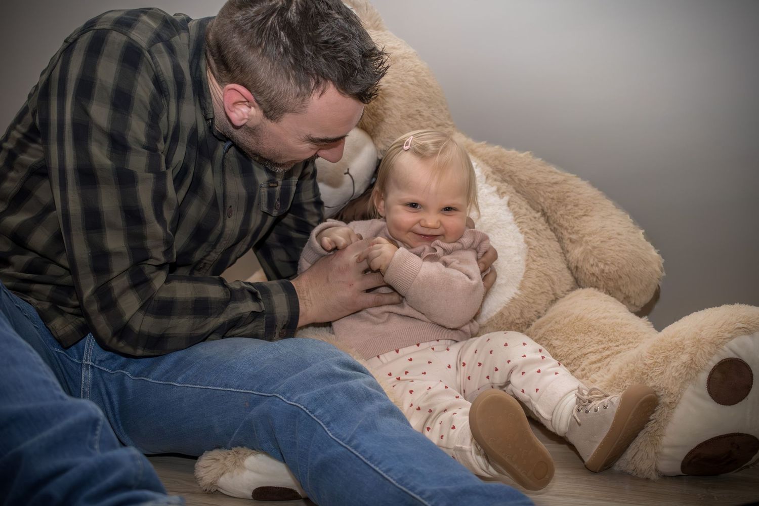 Parent and toddler share a tender playful moment while sitting with a large teddy bear.