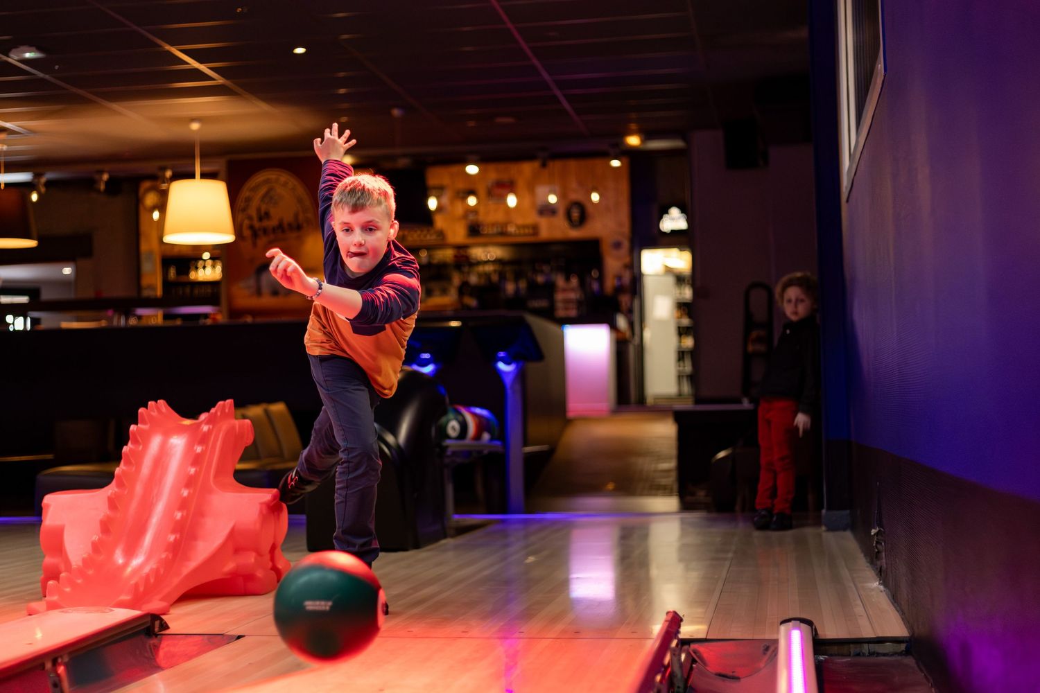 Young child bowling at a colorful indoor bowling alley, releasing the ball with enthusiasm.