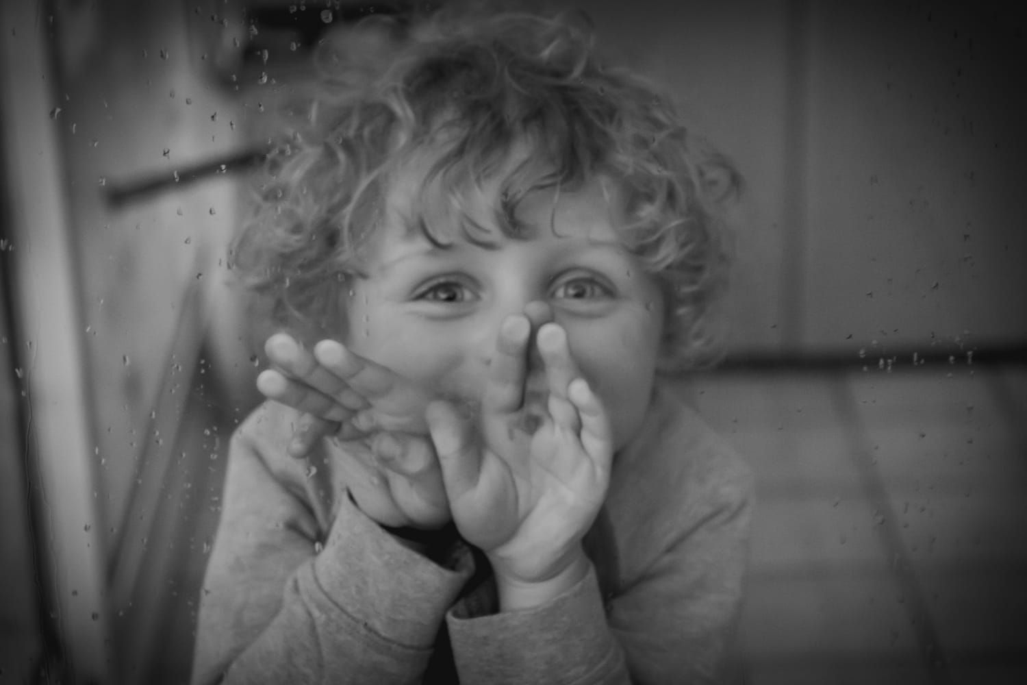Enfant derrière une vitre sur laquelle des gouttes de pluies coulent. Photo naturelle, non posée. Le regard d'un enfant vers son papa