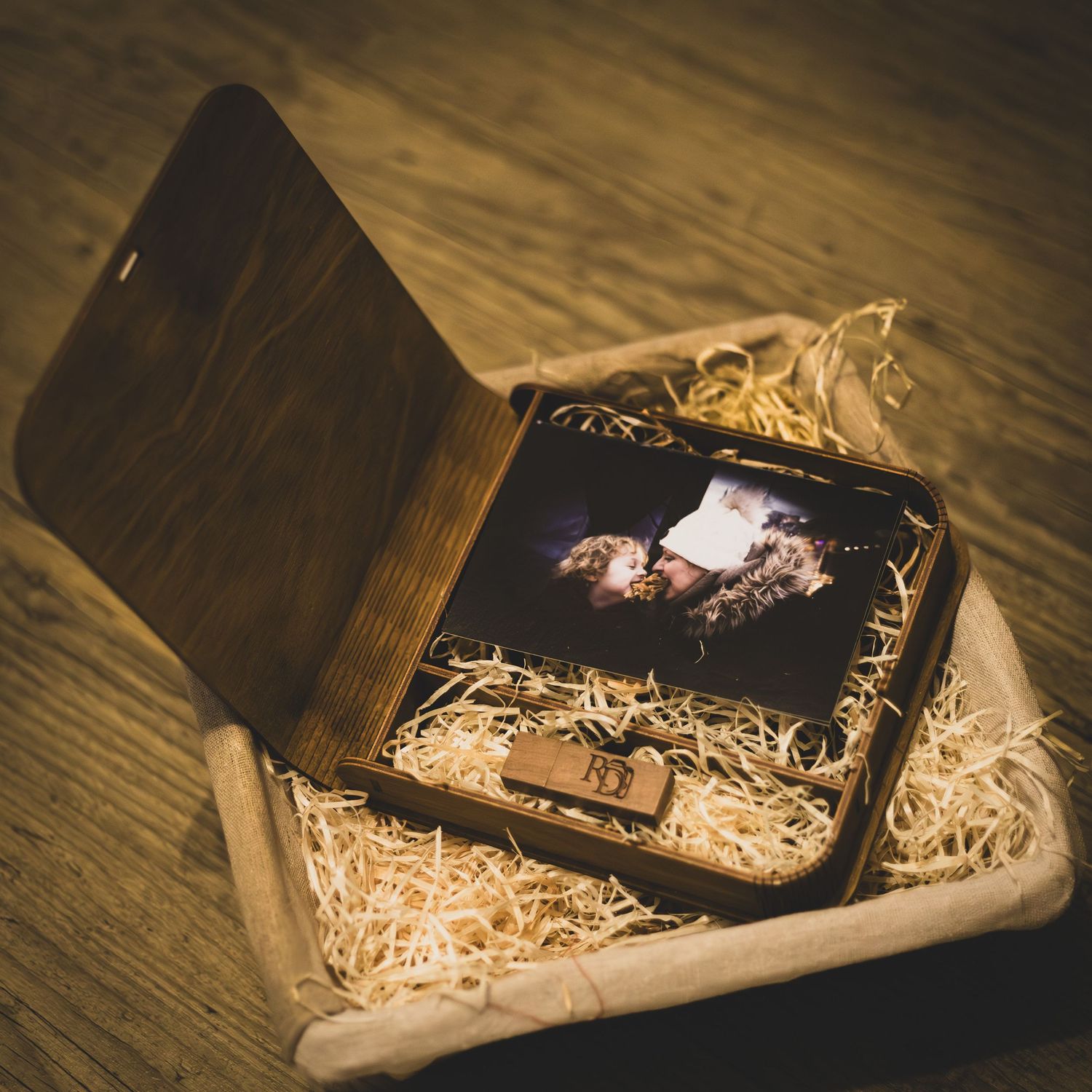 A small wooden box filled with decorative straw packaging sits on a rustic wooden surface in warm lighting.