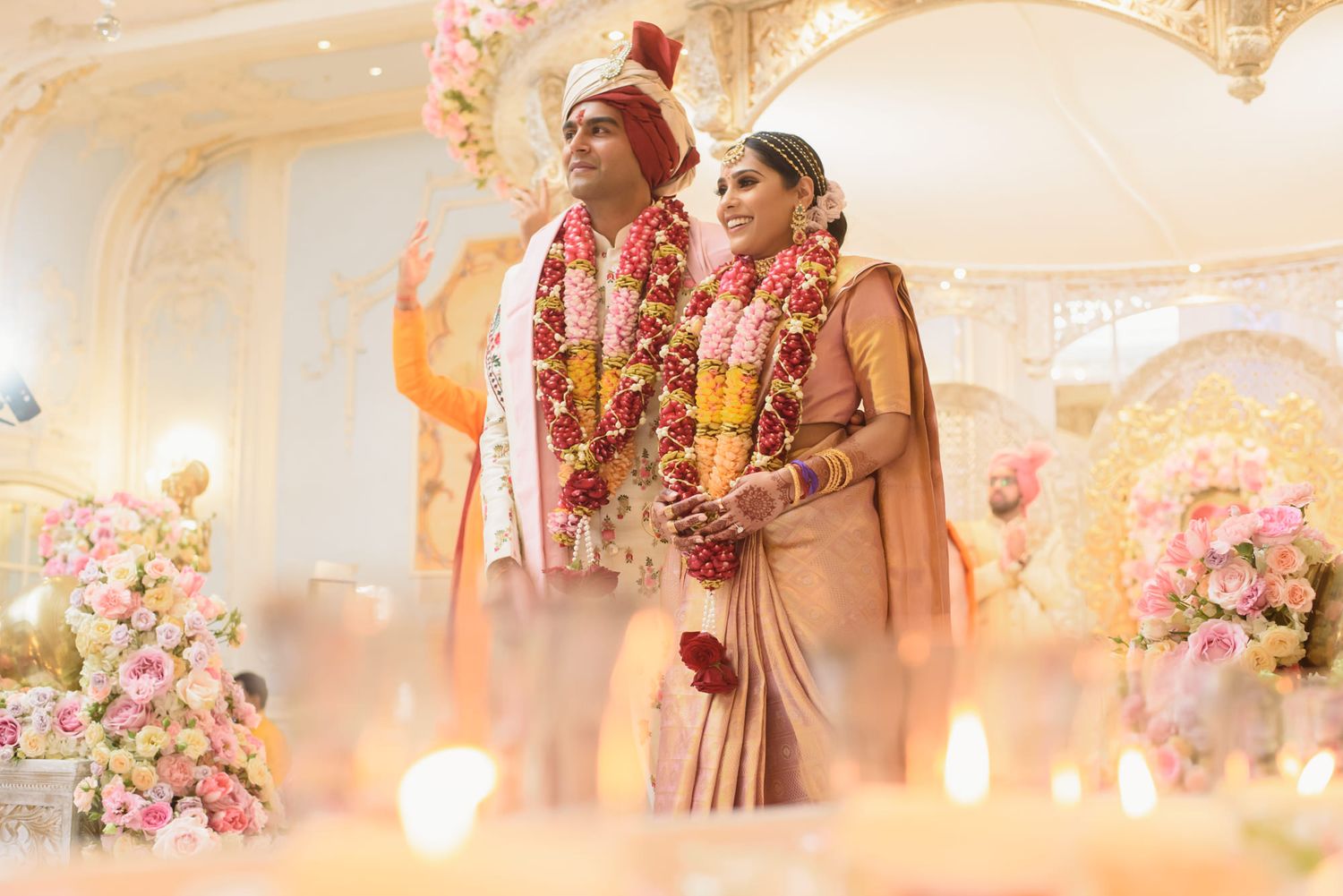 Indian bride and groom in traditional wedding attire standing together at elegantly decorated mandap.