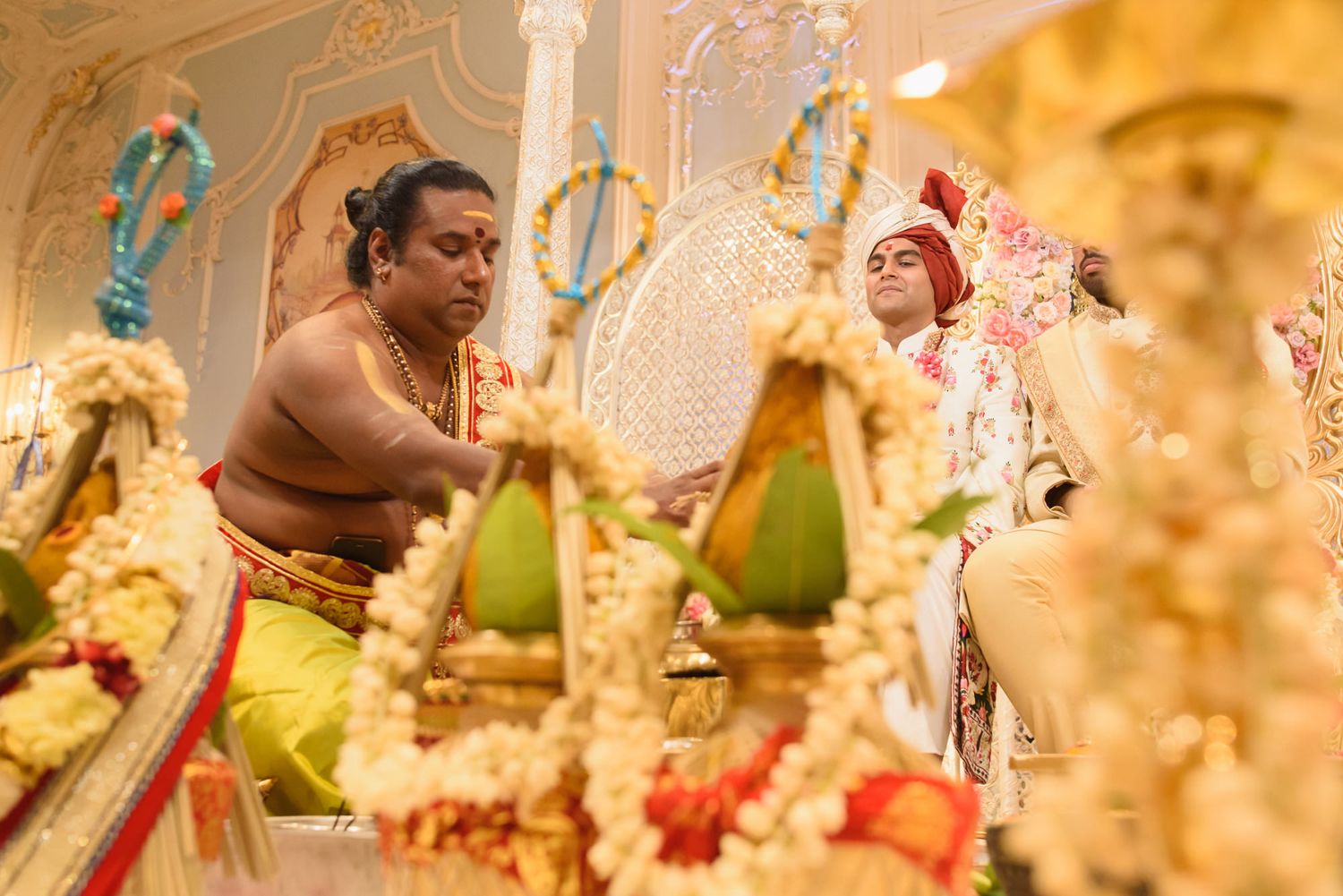 Hindu priest performs traditional wedding rituals surrounded by floral decorations at an Indian ceremony.