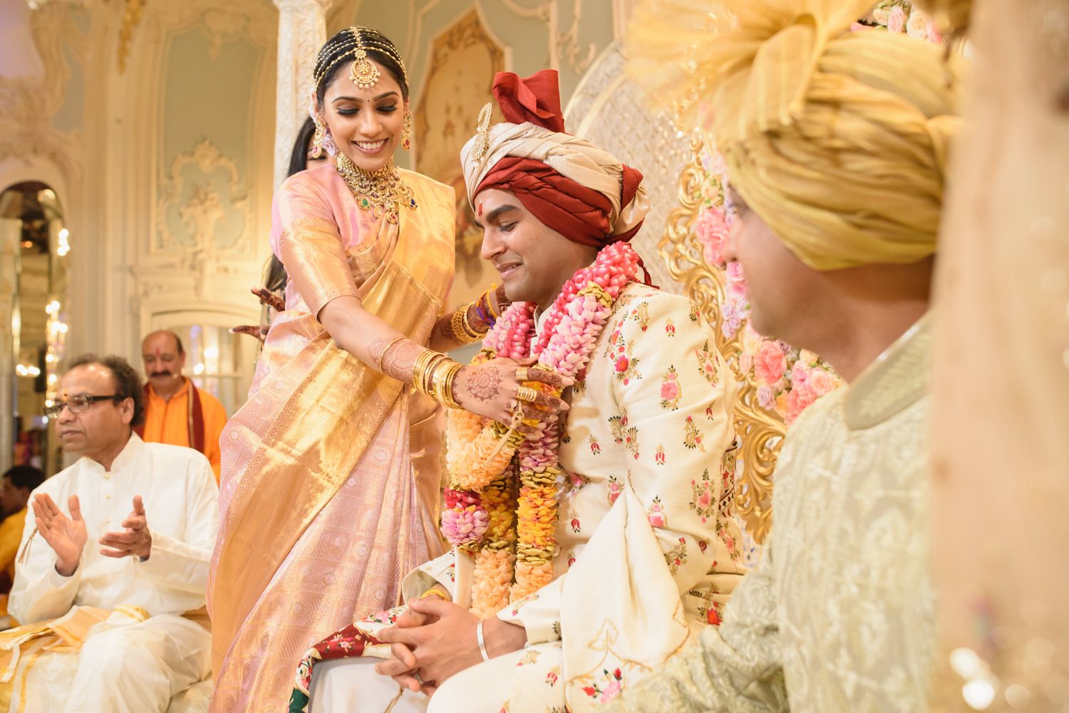 Bride in peach silk saree performs Hindu wedding ritual with groom at mandap.