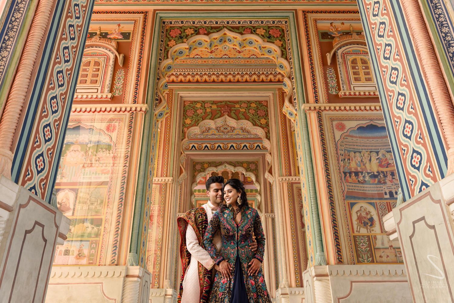 Couple in traditional Indian attire standing in beautifully frescoed palace archway in Jaipur.