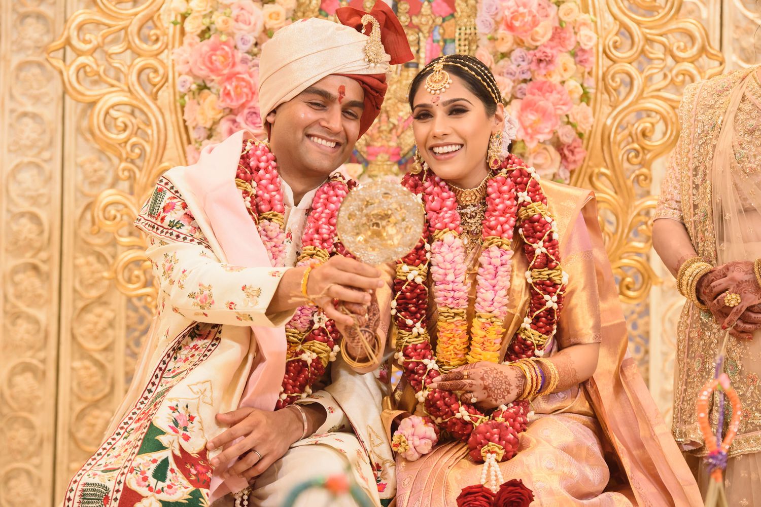 Smiling Hindu newlyweds in floral garlands pose together after wedding ceremony.
