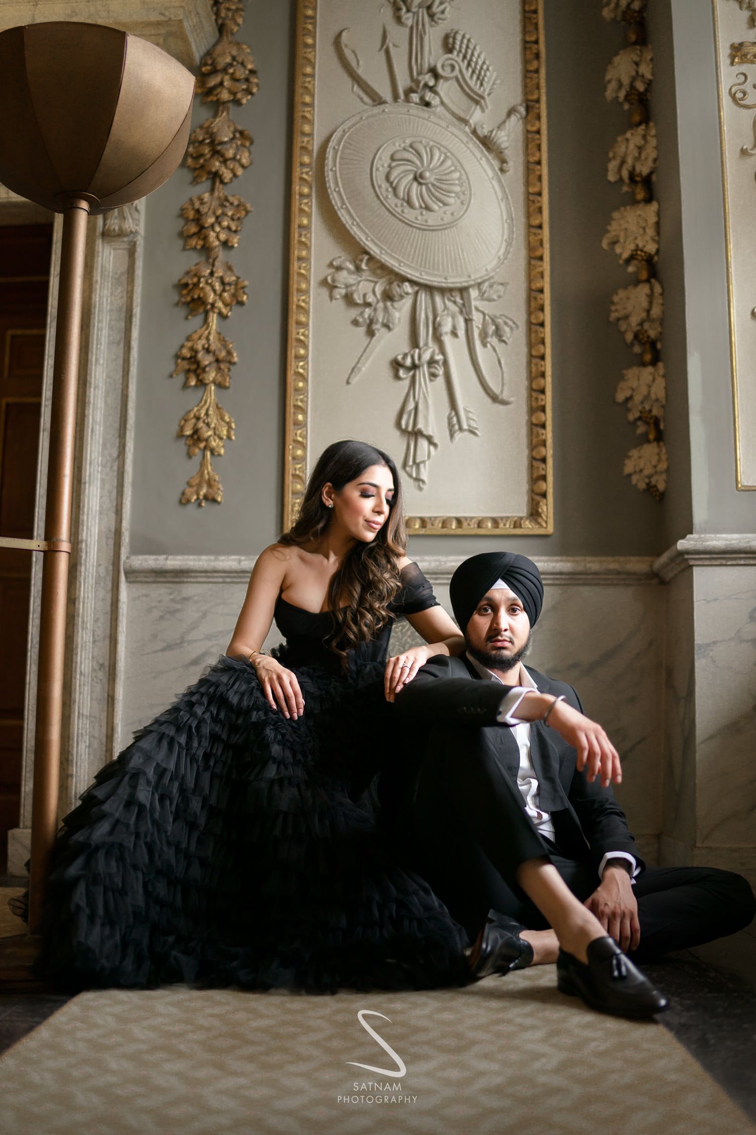 Indian couple in elegant black outfits posing in ornate marble interior for pre-wedding shoot.