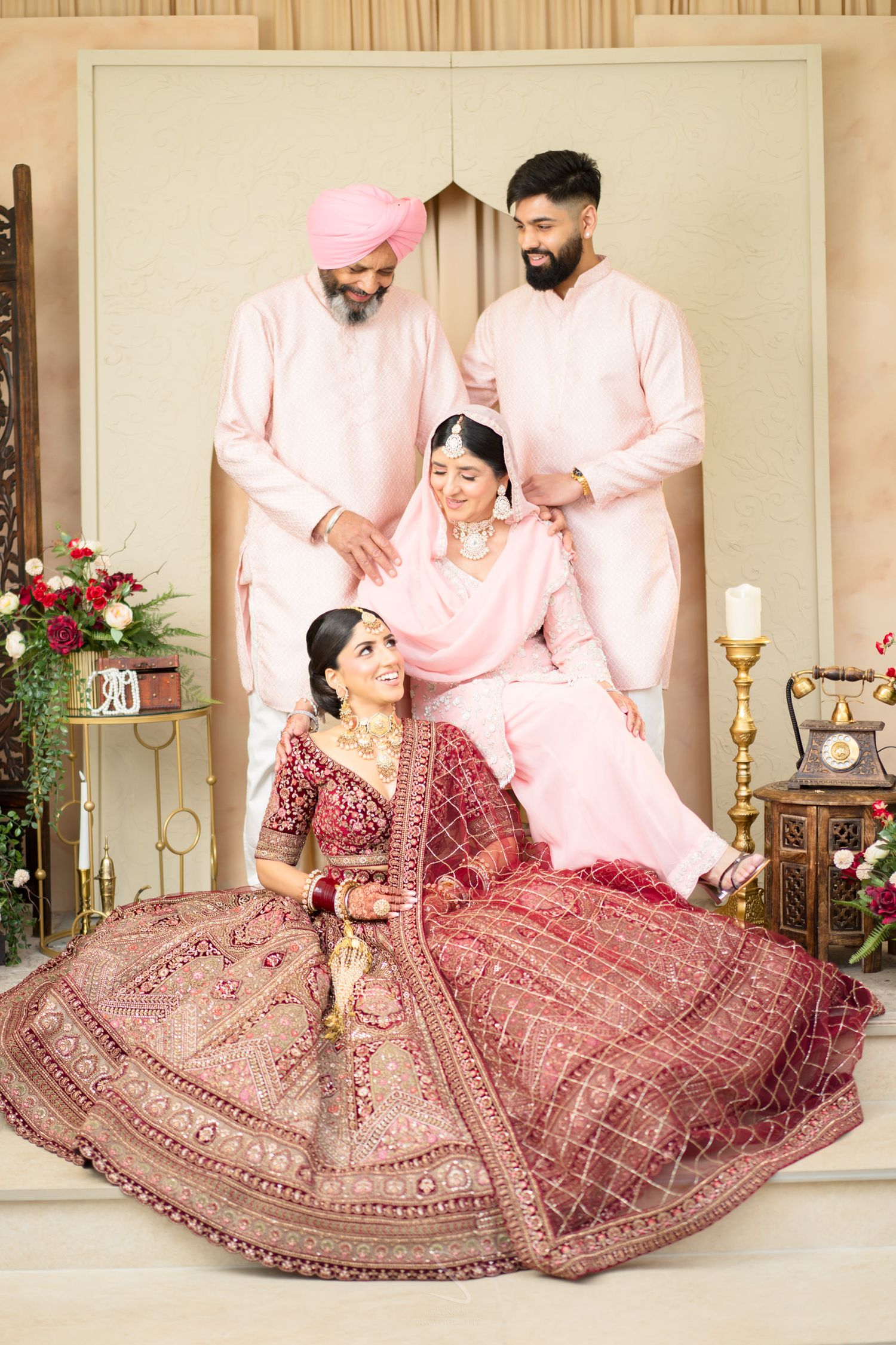 Sikh bride in red lehenga poses with family members in pink traditional Indian wedding attire.