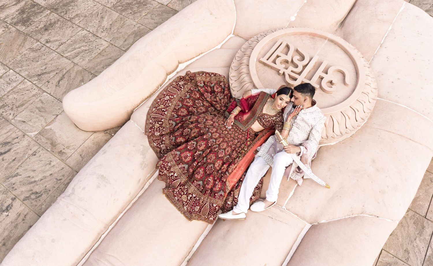 Couple in traditional Indian wedding attire posing on decorative heart-shaped backdrop at elegant venue.
