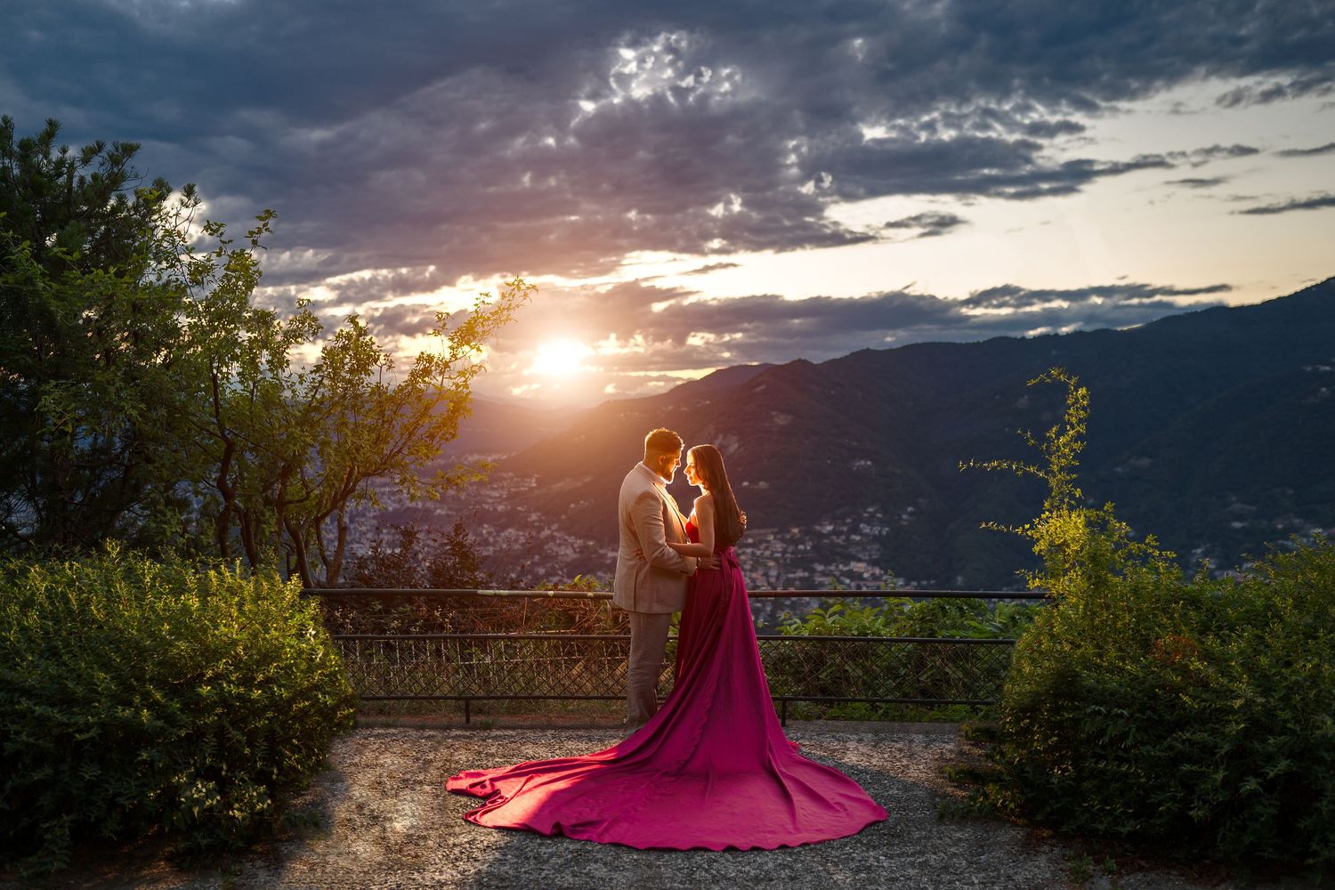 Bride in red gown and groom embrace at sunset with mountain views.