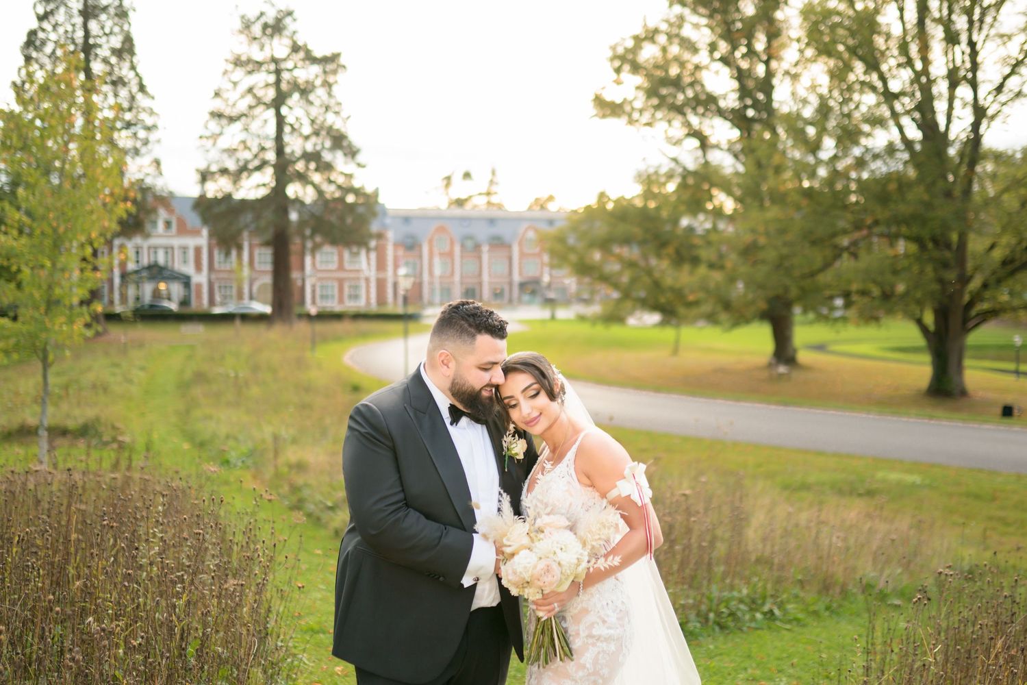 Romantic bride and groom portrait on lush green grounds with elegant manor house in background.