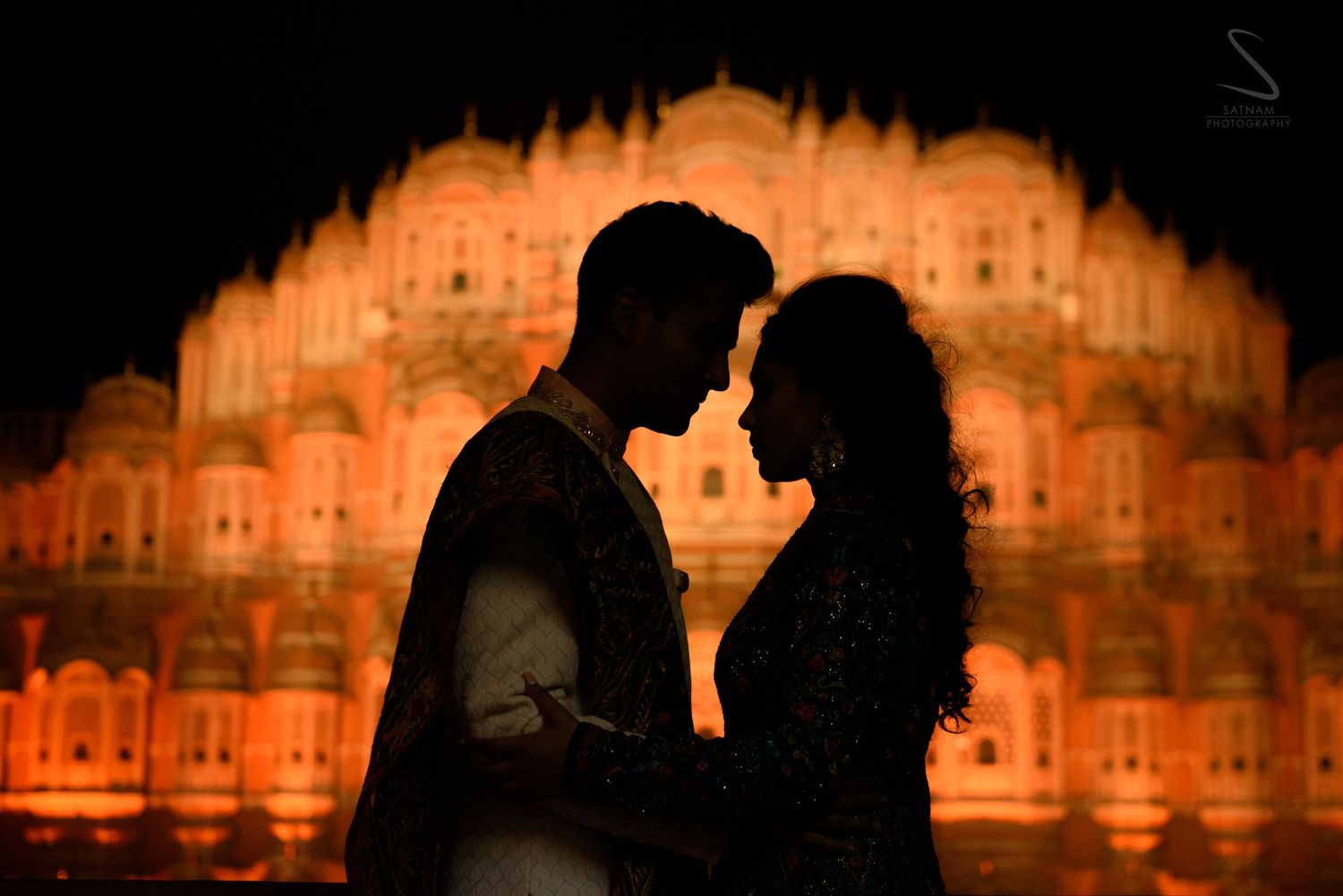 Romantic couple silhouetted against glowing Hawa Mahal facade at night in Jaipur.