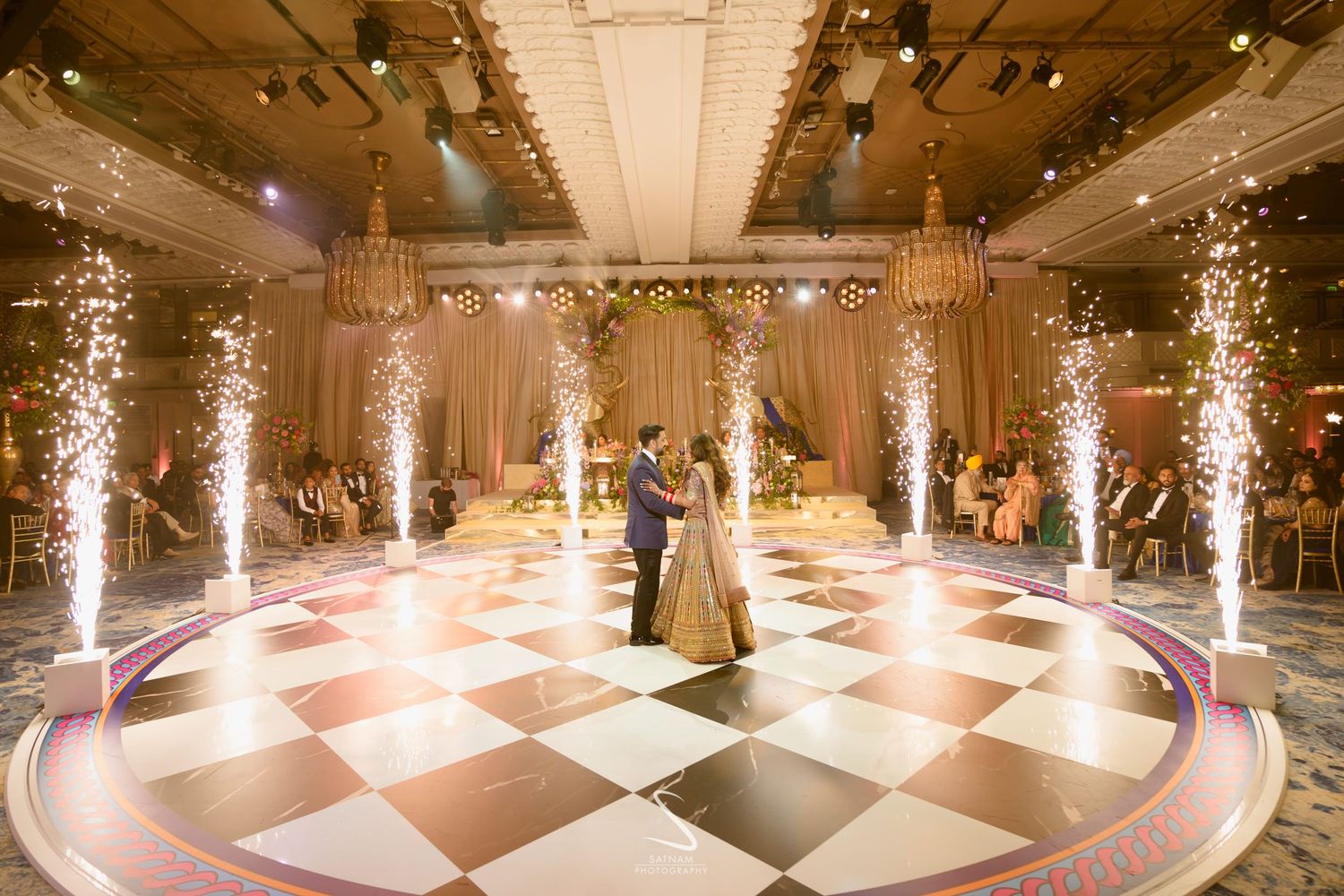 Couple sharing first dance on checkered floor with sparkling pyrotechnics at elegant wedding reception.