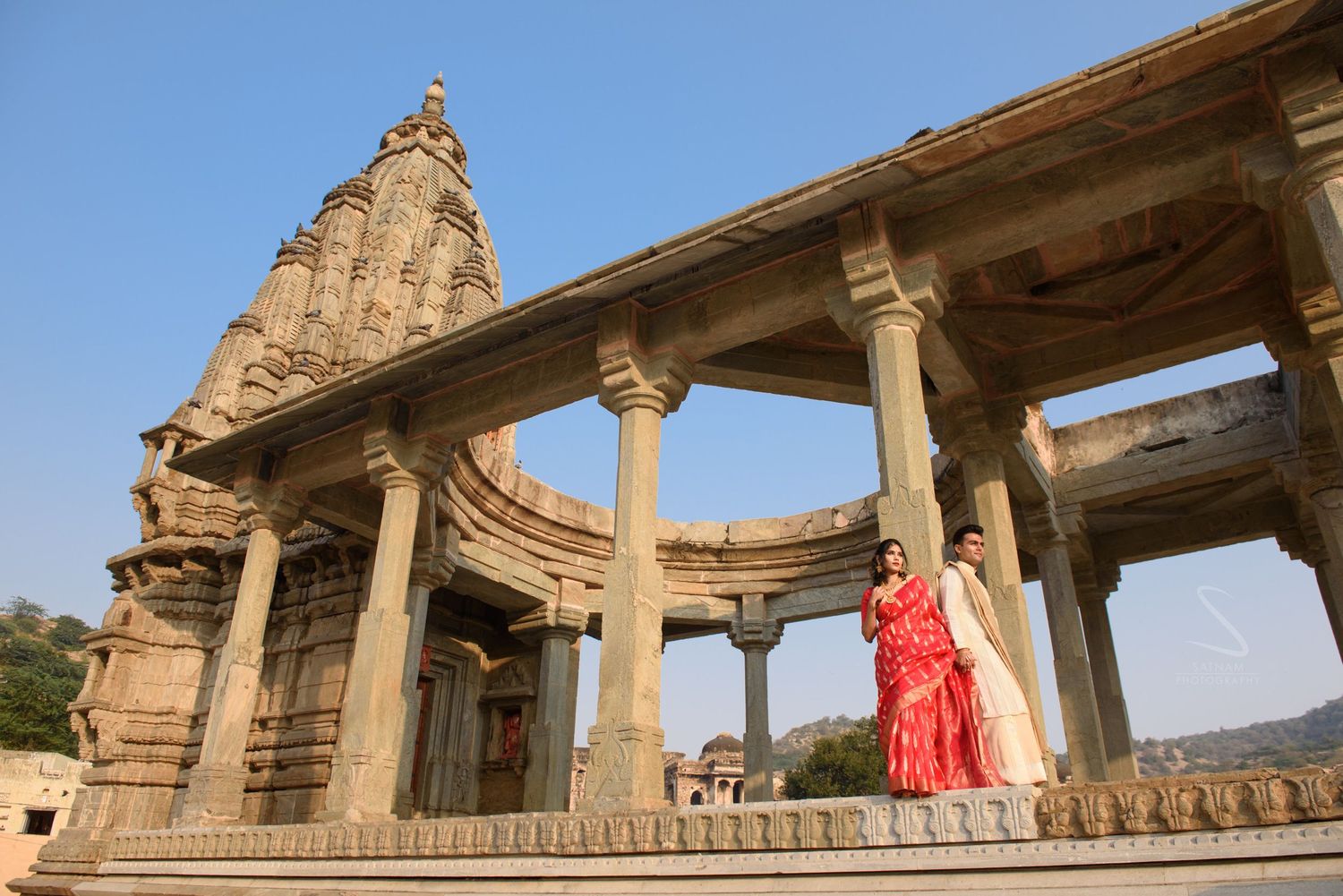 Couple in traditional Indian attire posing at an ornate ancient Hindu temple with stone columns.