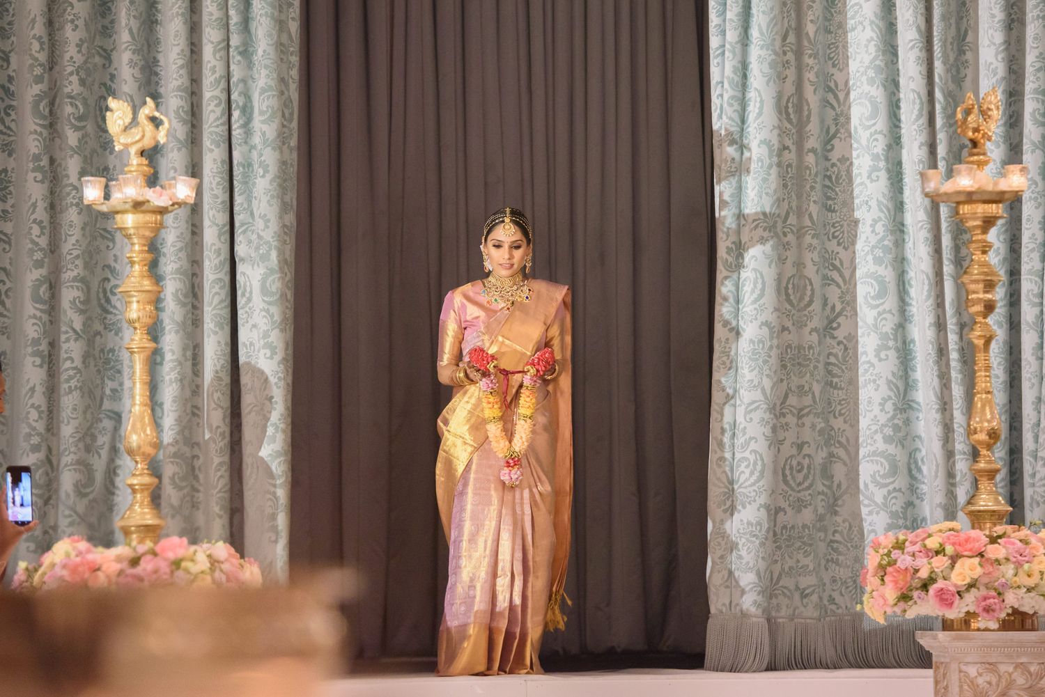 Bride in golden silk saree walks down aisle at traditional Indian wedding ceremony.