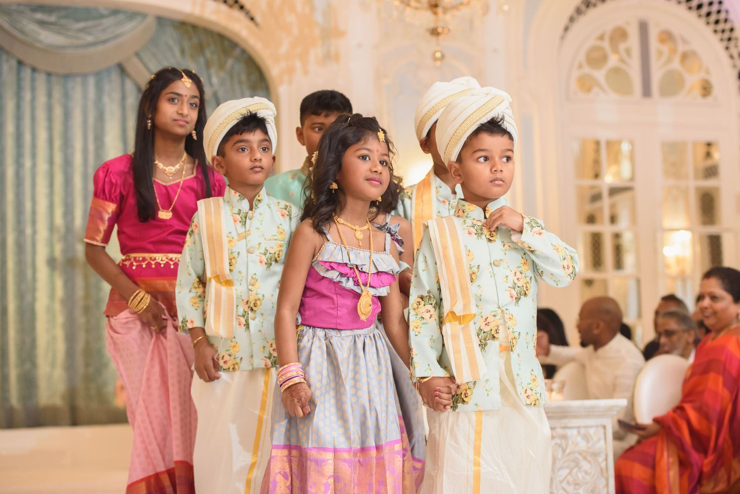 Children dressed in traditional Indian wedding attire walk together during elegant Hindu wedding celebration.
