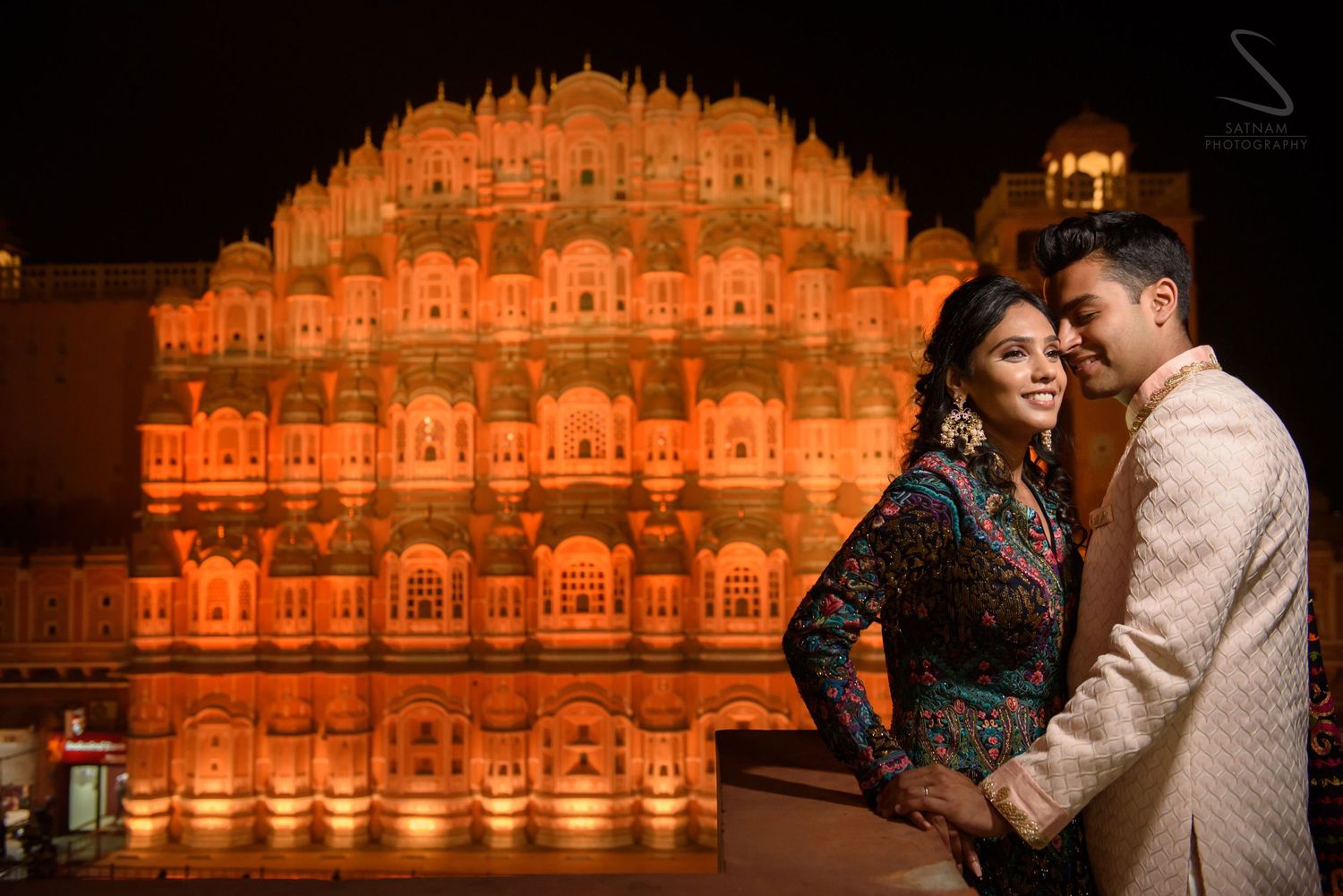 Couple embracing at night in front of illuminated Hawa Mahal palace in Jaipur.