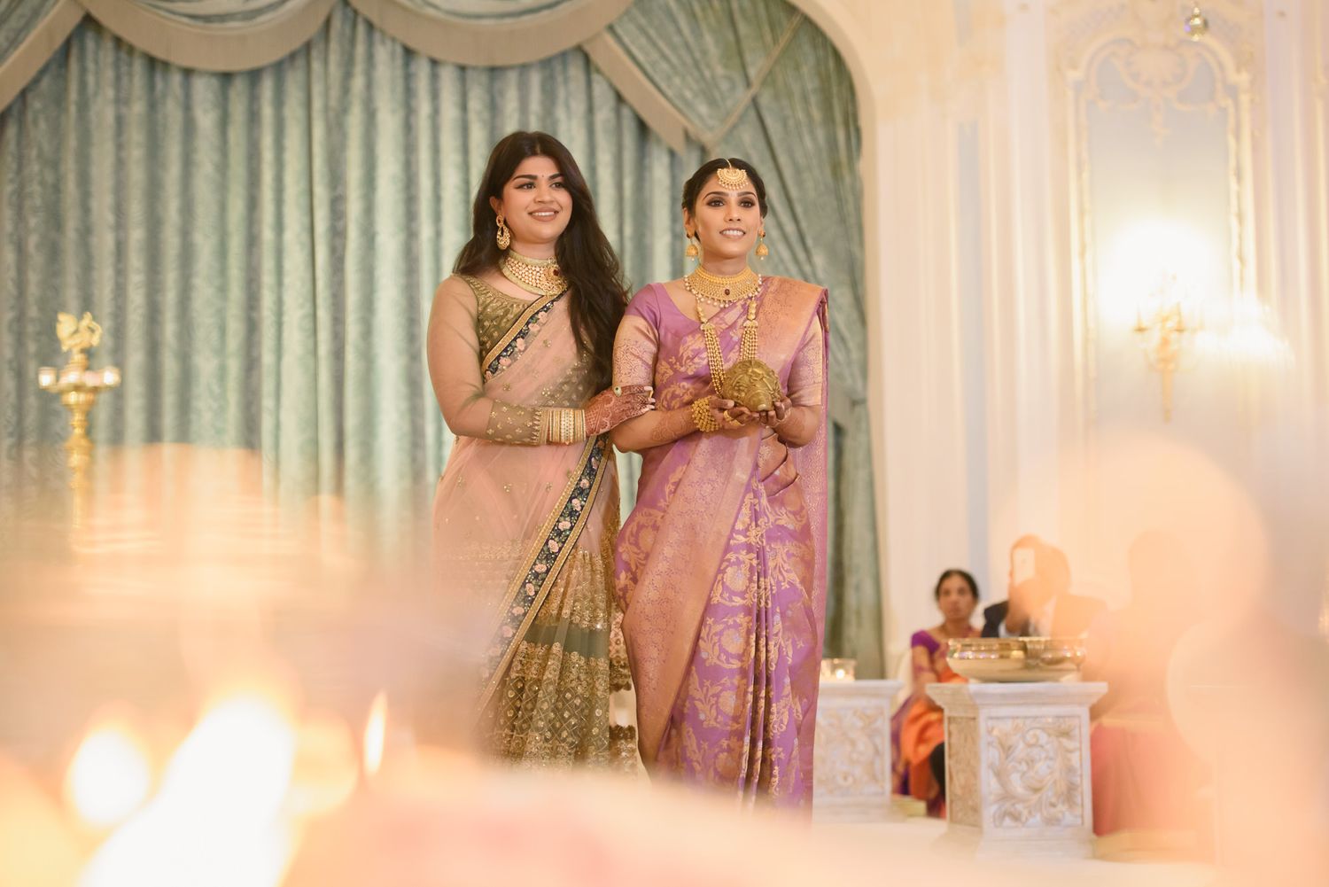 Two women in traditional Indian attire stand together during a Hindu wedding ceremony with candles.