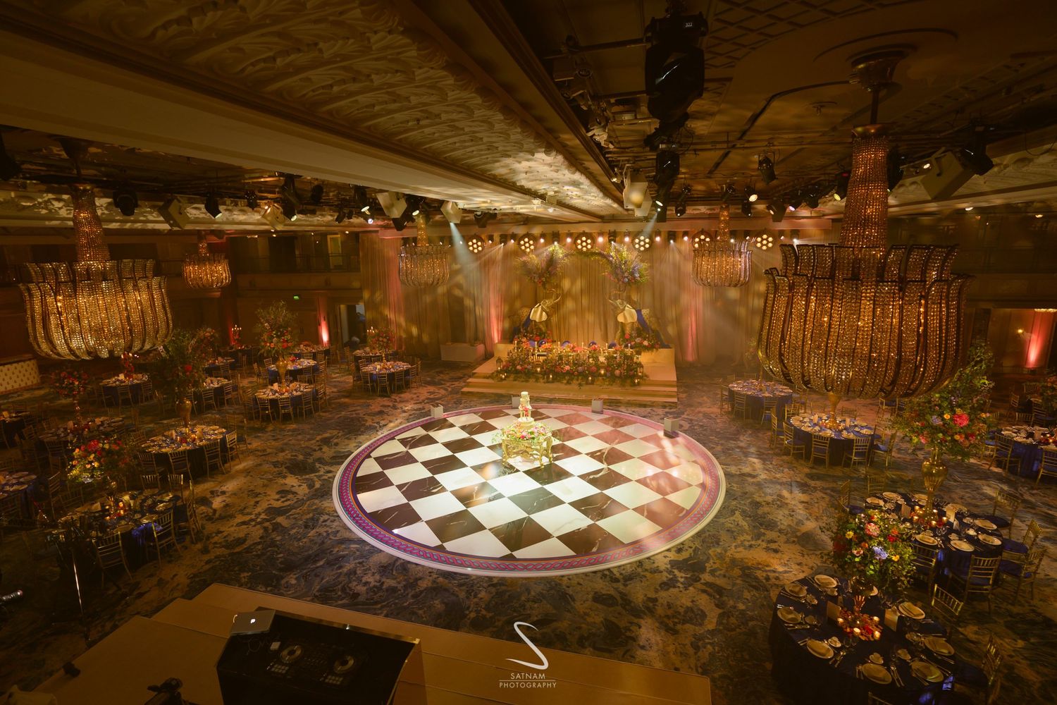 Stunning wedding reception venue with checkered dance floor, ornate decor, dramatic lighting and floral arrangements.