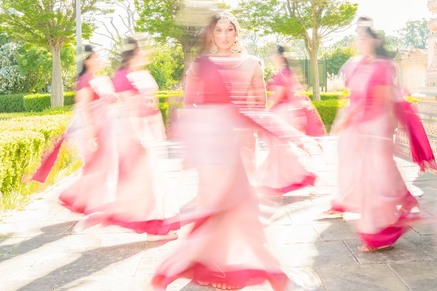 Motion blur artistic photo of dancers in pink outfits performing at an outdoor Indian wedding celebration.