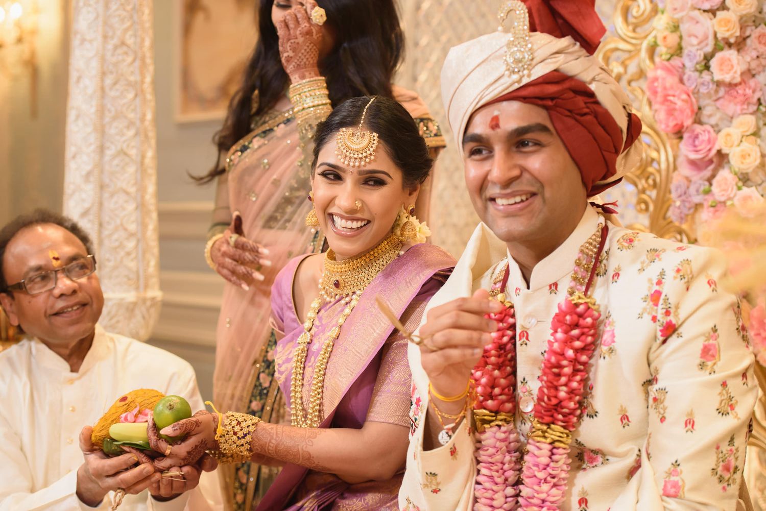 Indian bride and groom smile holding ceremonial items during traditional Hindu wedding celebration.