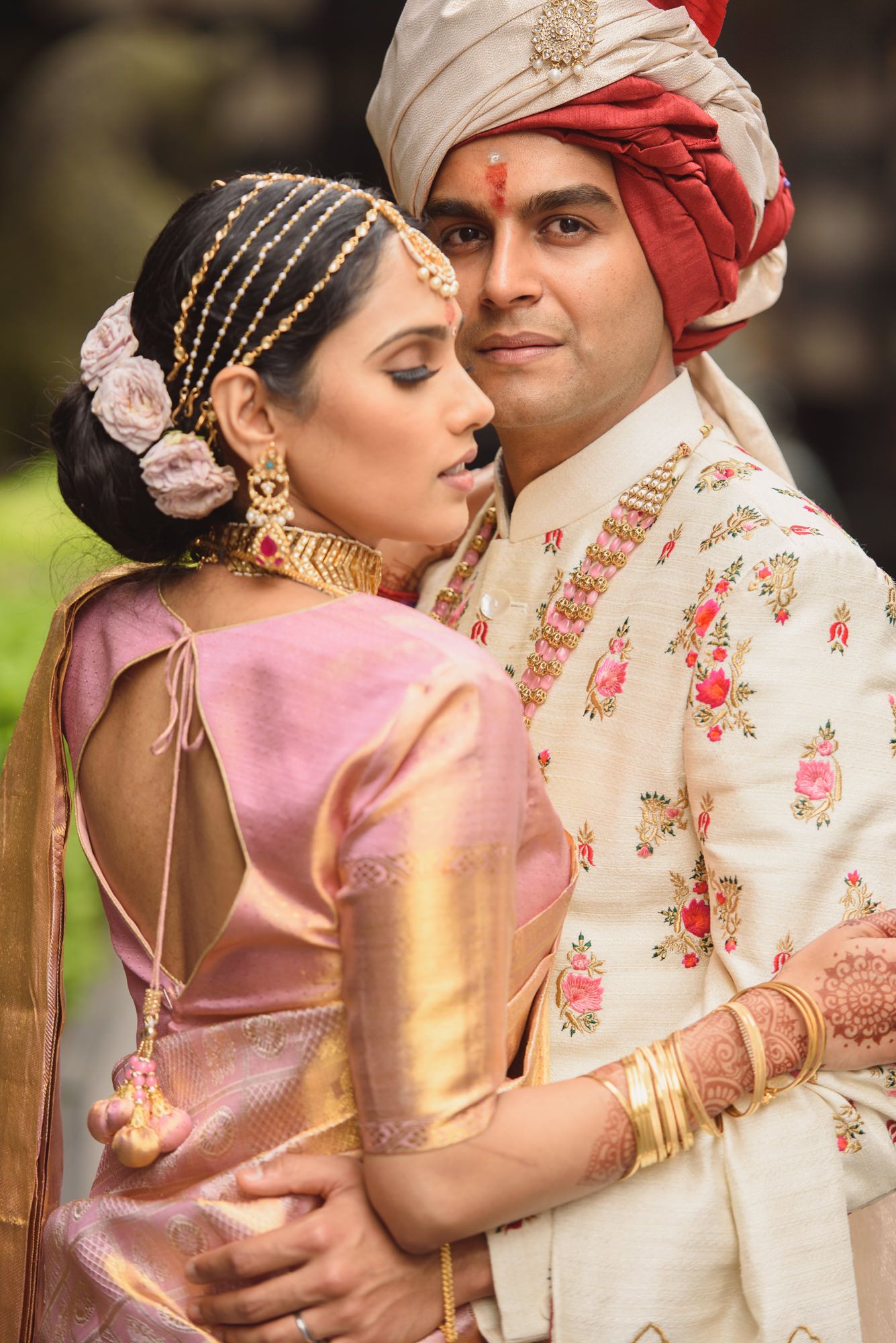 Indian bride in pink Paithani saree embracing groom in embroidered sherwani at traditional wedding.