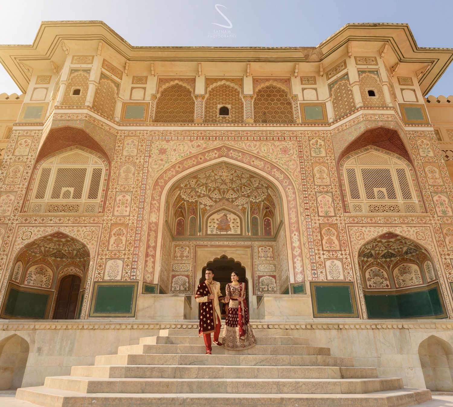 Couple in traditional Indian attire walking through ornate Amber Fort gateway in Jaipur, Rajasthan.