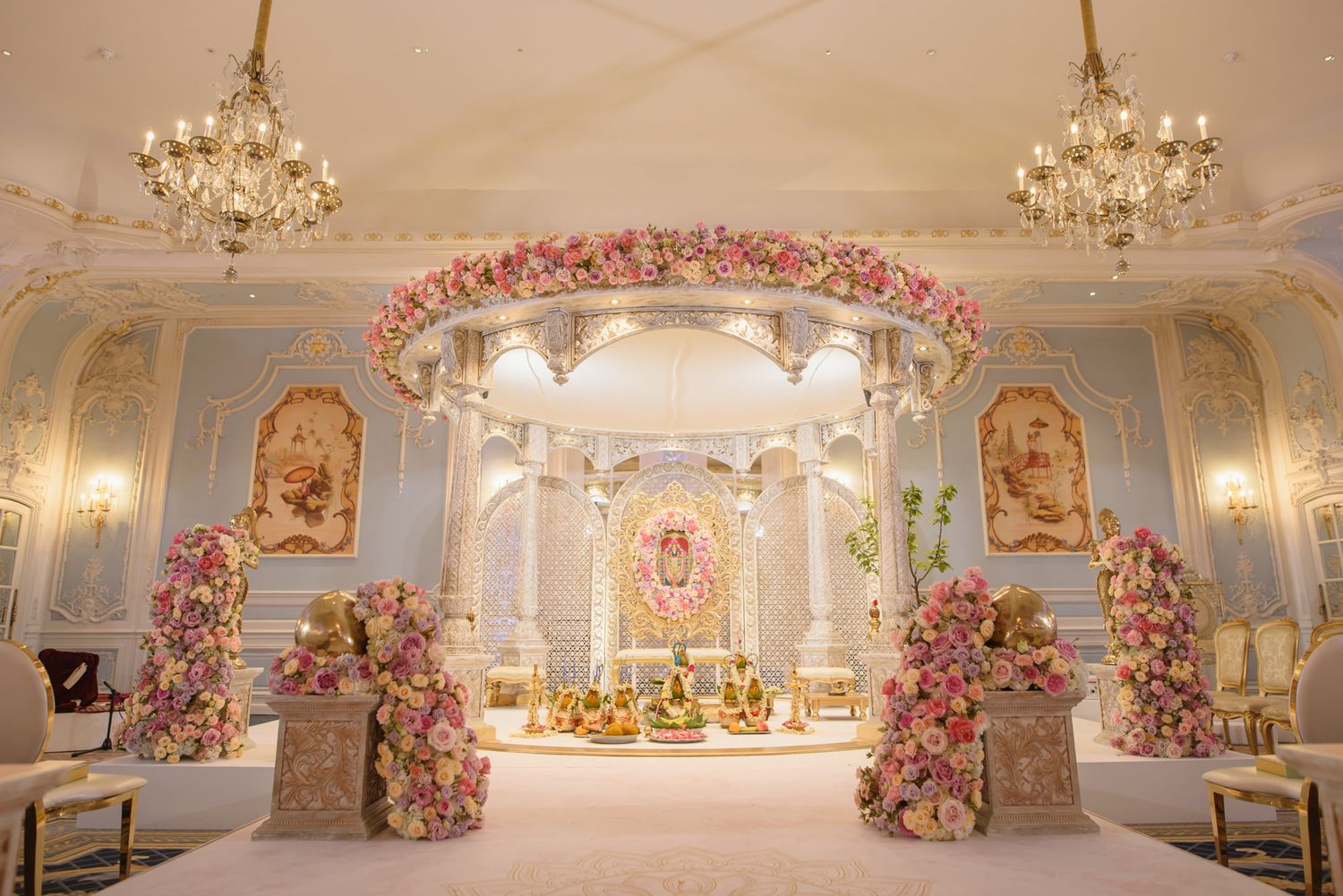Luxurious Indian wedding mandap with pink floral arrangements, gold chandeliers, and ornate white decor.