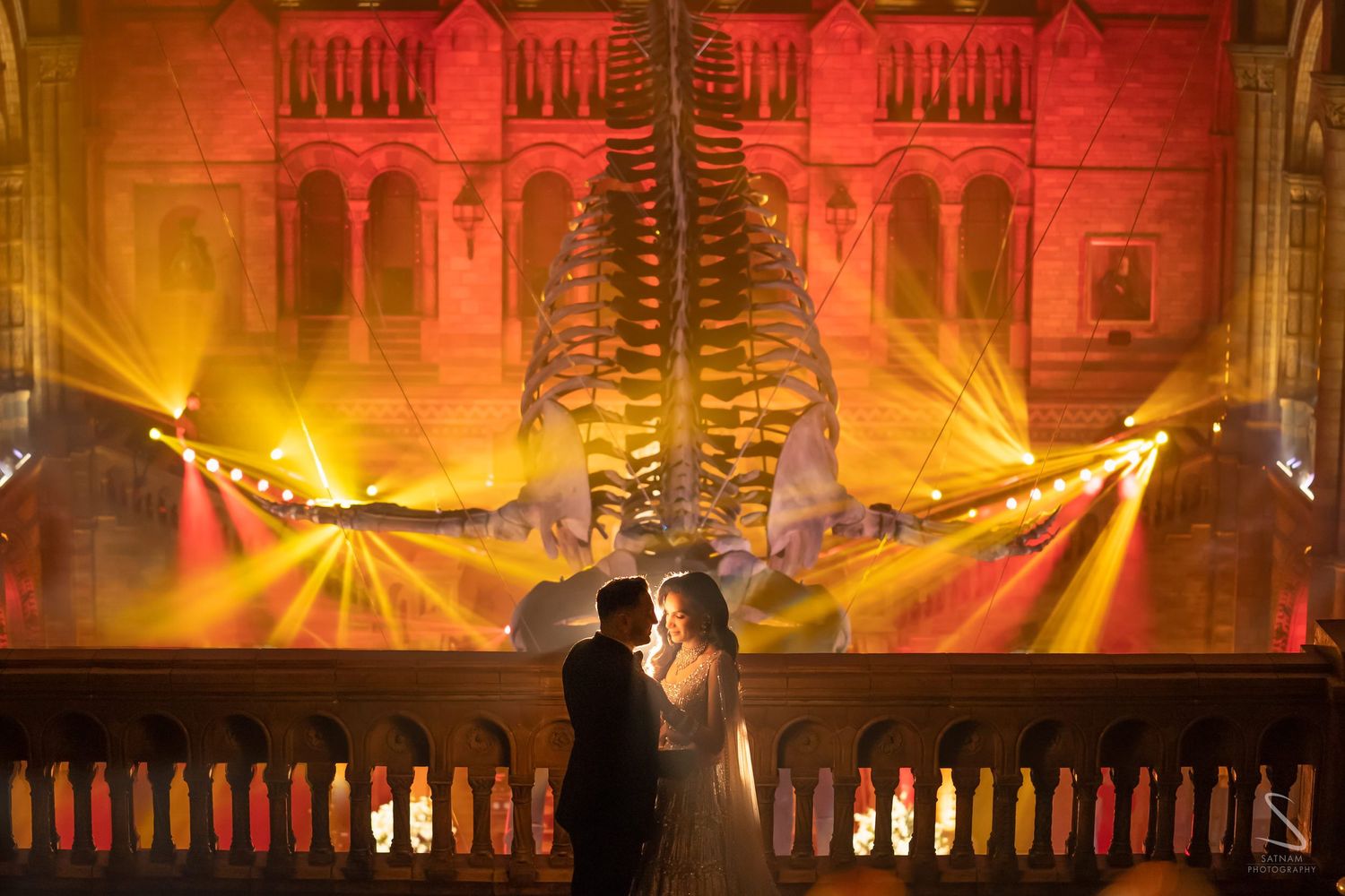 Bride and groom silhouetted against dramatic golden light show at Natural History Museum wedding reception.