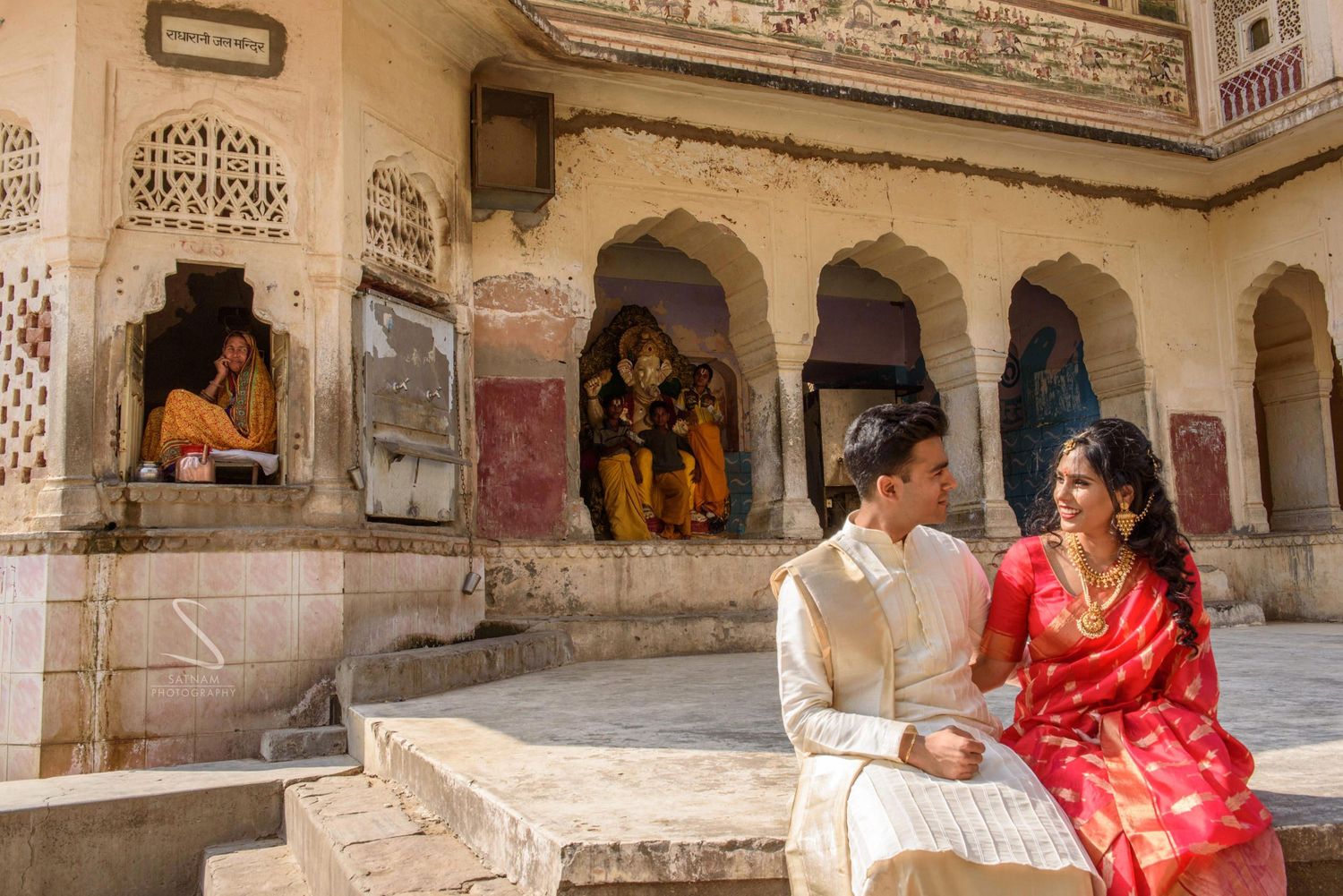 Couple in traditional Indian wedding outfits sitting near an ancient temple shrine in Rajasthan.