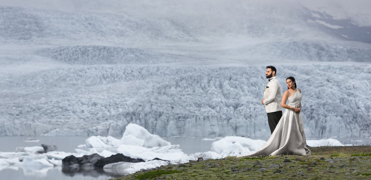 Couple in wedding attire posing before a glacier and icy lagoon in Iceland.