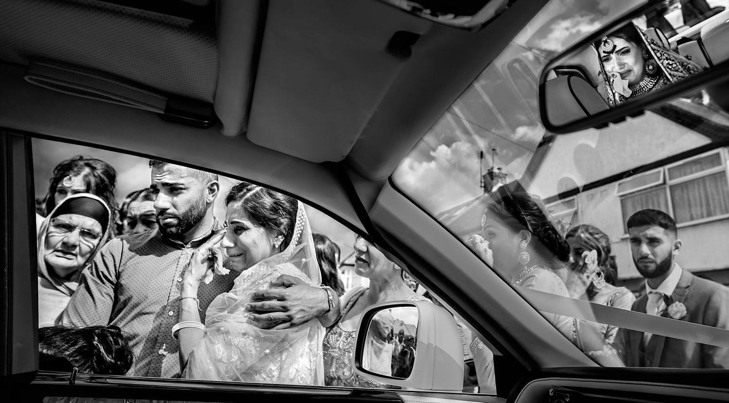Black and white wedding photo of bride and groom seen through car windows.