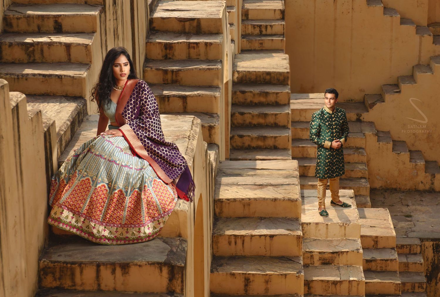 Bride in colorful lehenga and groom pose on ancient stepwell stairs in Jaipur, India.