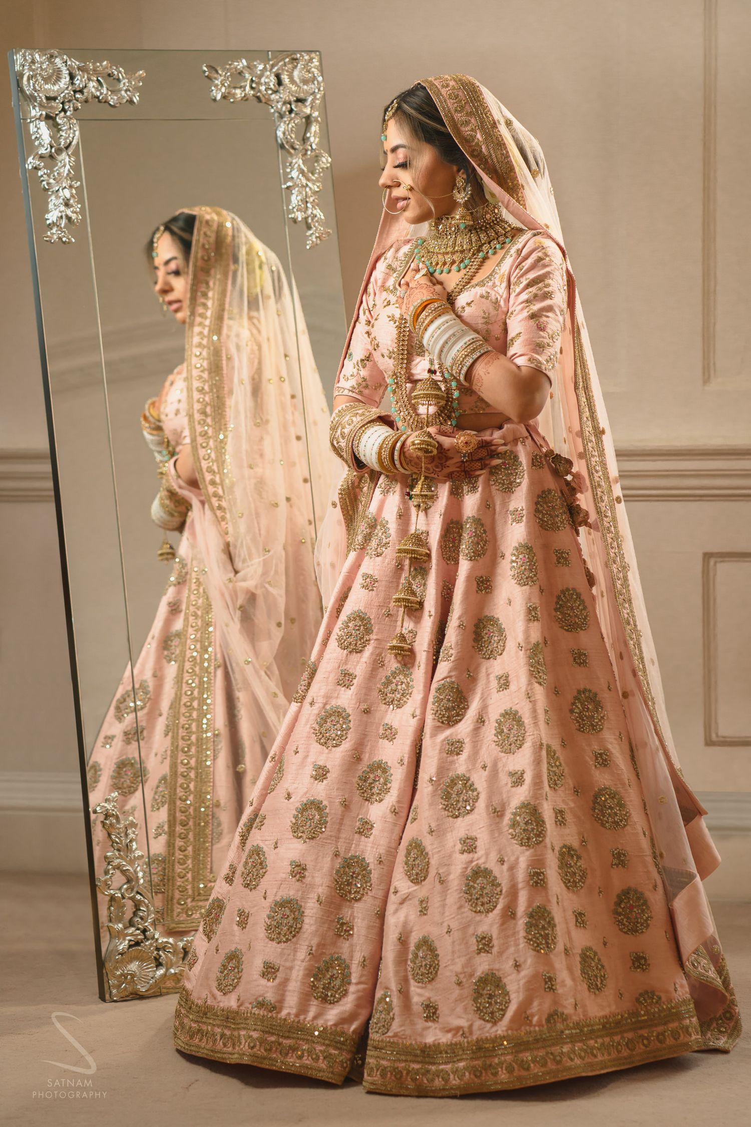 Indian bride in pink embroidered lehenga admiring her reflection in a full-length mirror.