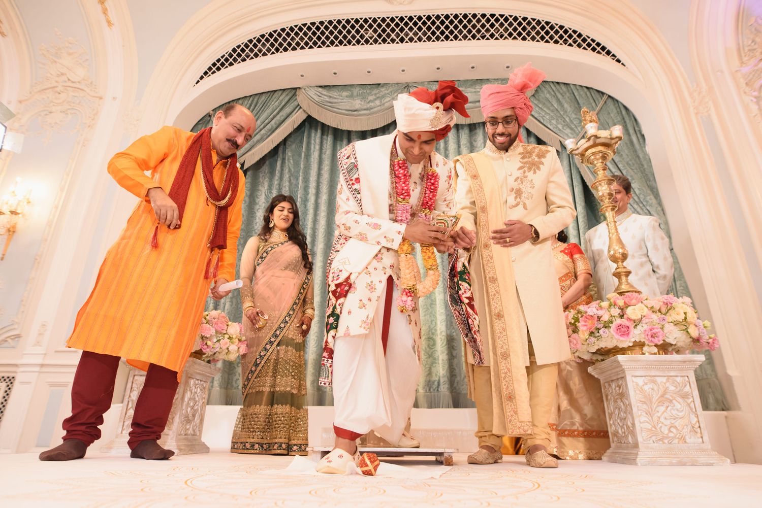 Indian groom in floral sherwani performs traditional Hindu wedding ceremony rituals at ornate mandap.