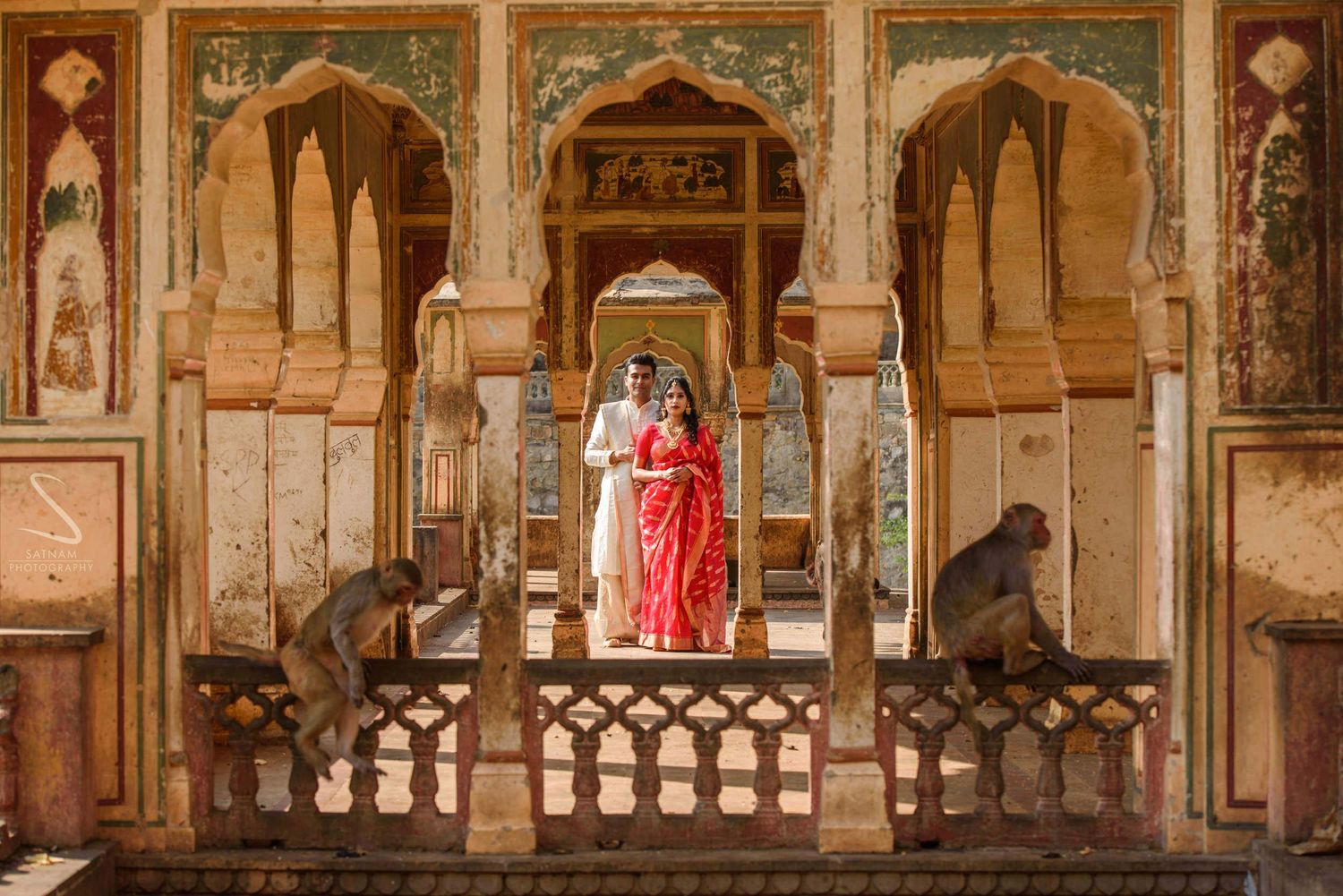 Indian wedding couple stands on a balcony of a colorful temple surrounded by monkeys in Jaipur.