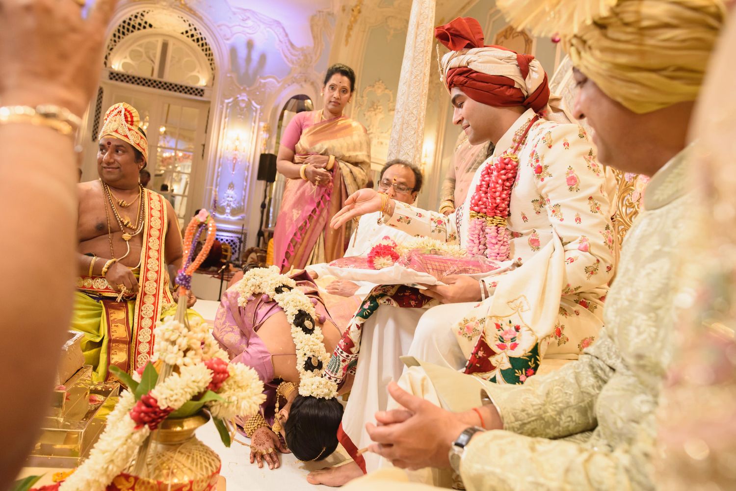 Hindu priest performs sacred rituals as wedding guests bow respectfully at ornate Indian wedding ceremony.