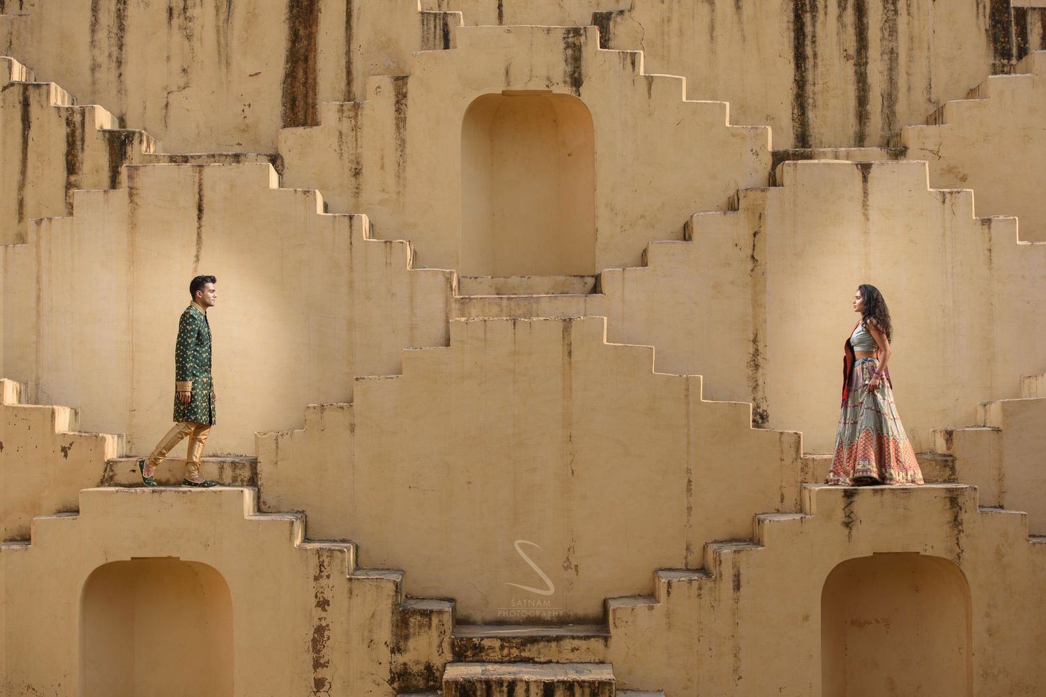 Couple in traditional Indian attire poses on geometric sandstone steps of a historic stepwell in Jaipur.