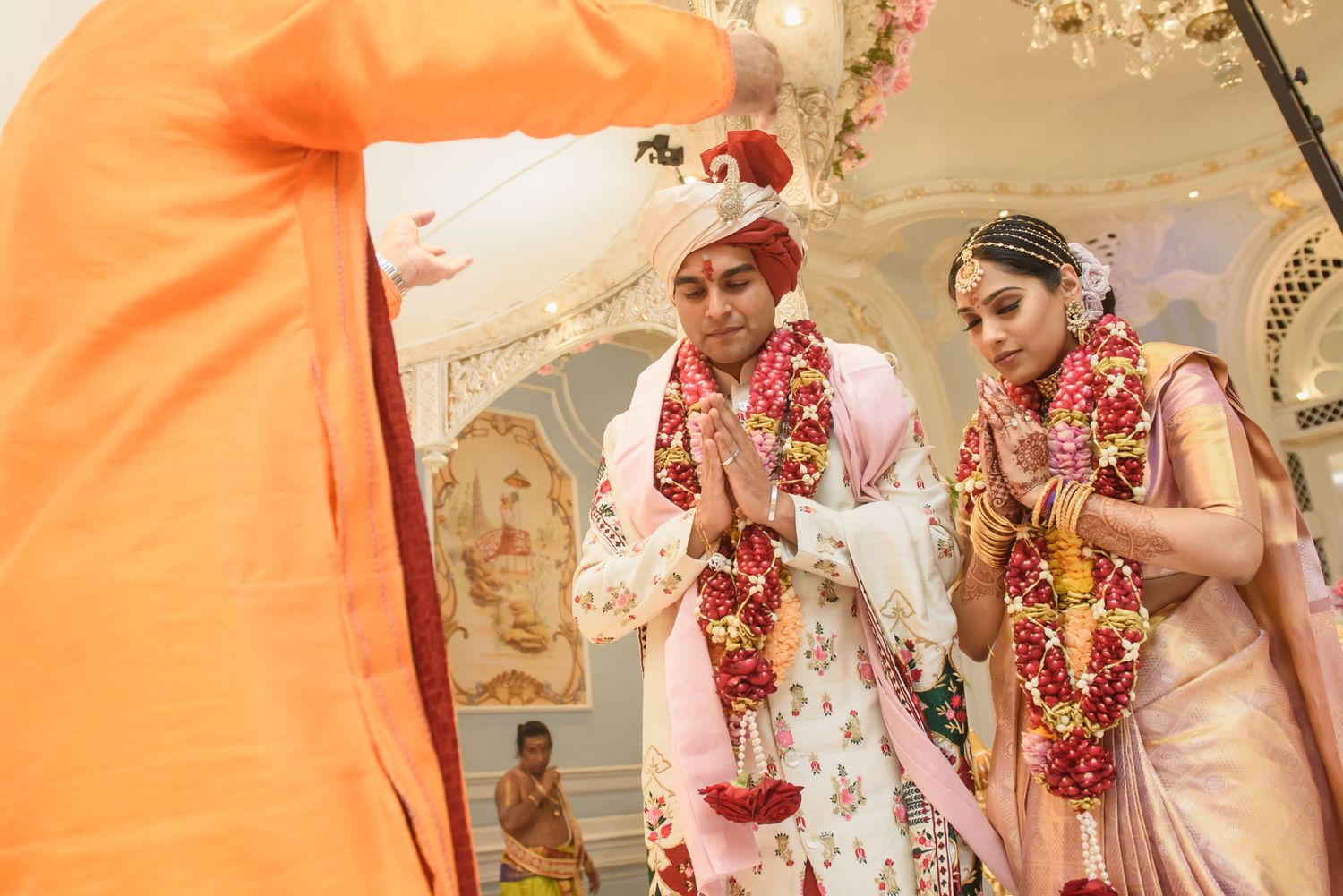Hindu bride and groom in traditional attire performing wedding rituals before priest at ornate mandap.