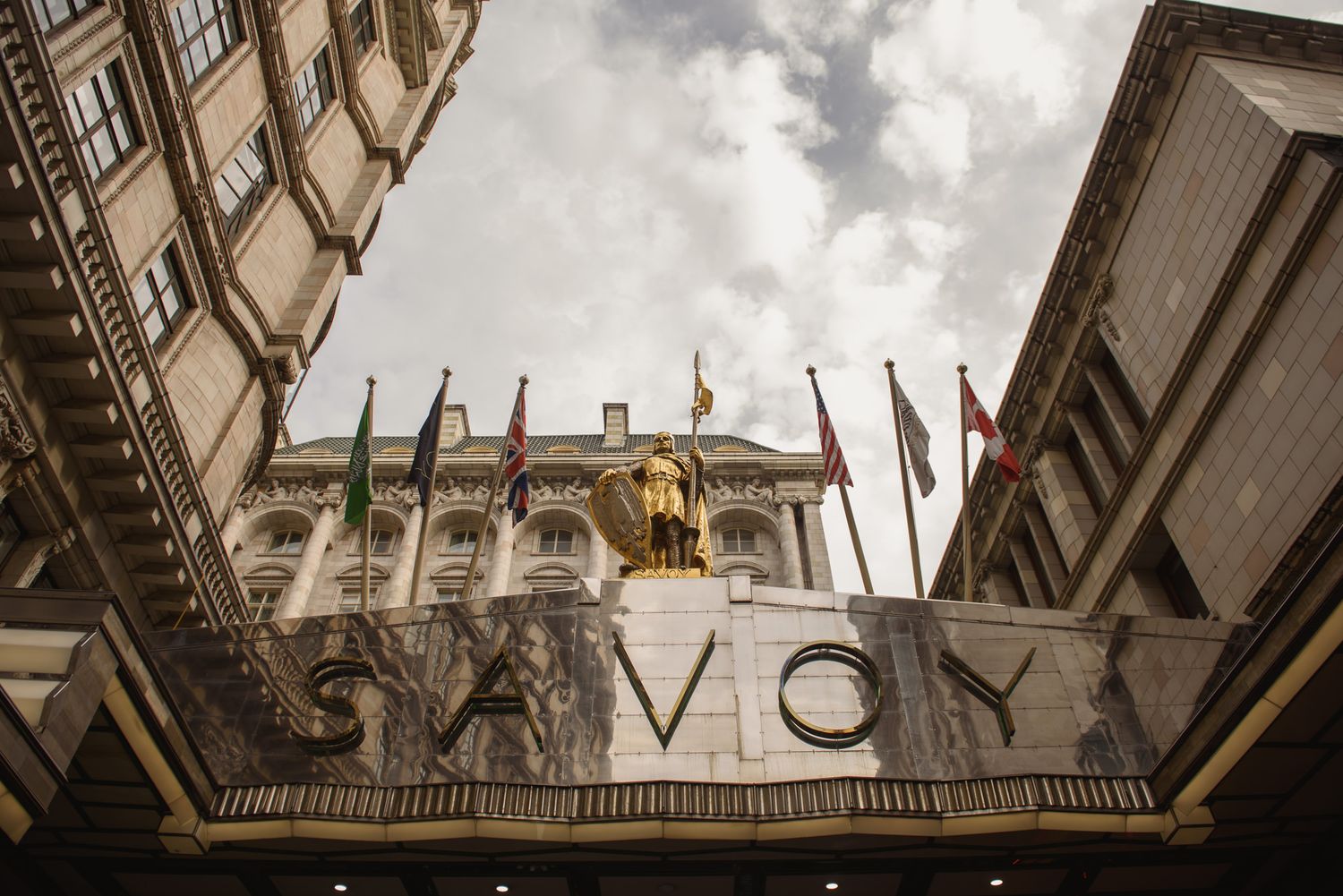 Iconic facade of The Savoy luxury hotel in London with golden statue and international flags.