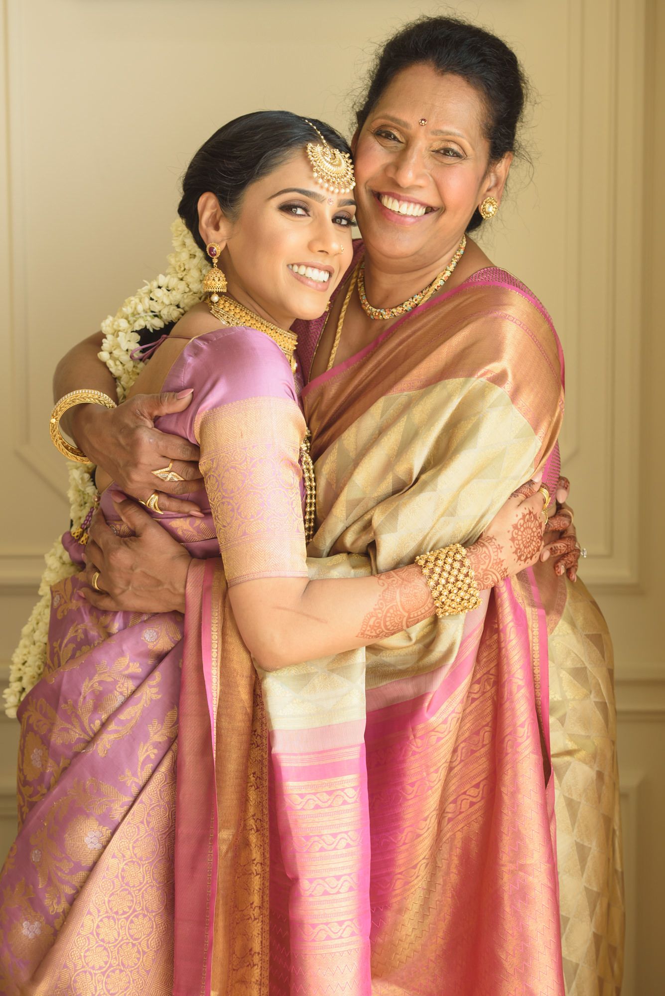 South Indian bride in purple silk saree and gold jewelry shares warm embrace with mother at wedding.