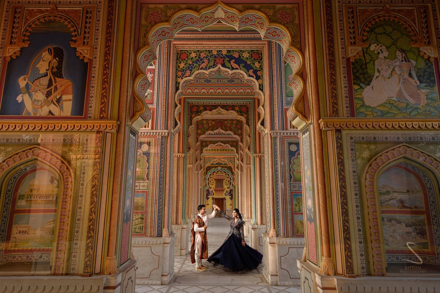 Couple in traditional attire posing in ornate painted corridor of Patrika Gate, Jaipur.