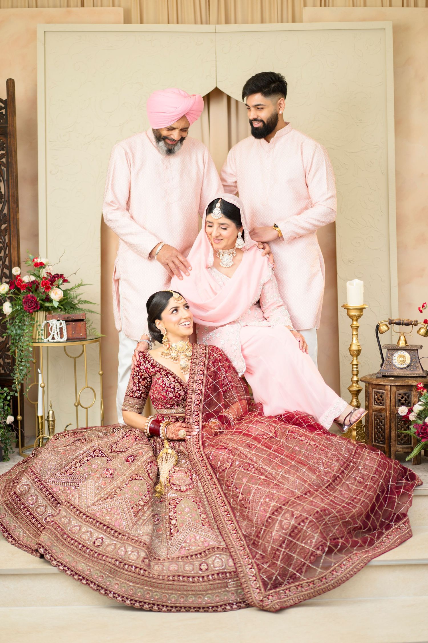 Sikh bride in red embroidered lehenga seated with family members in pink outfits at traditional wedding.