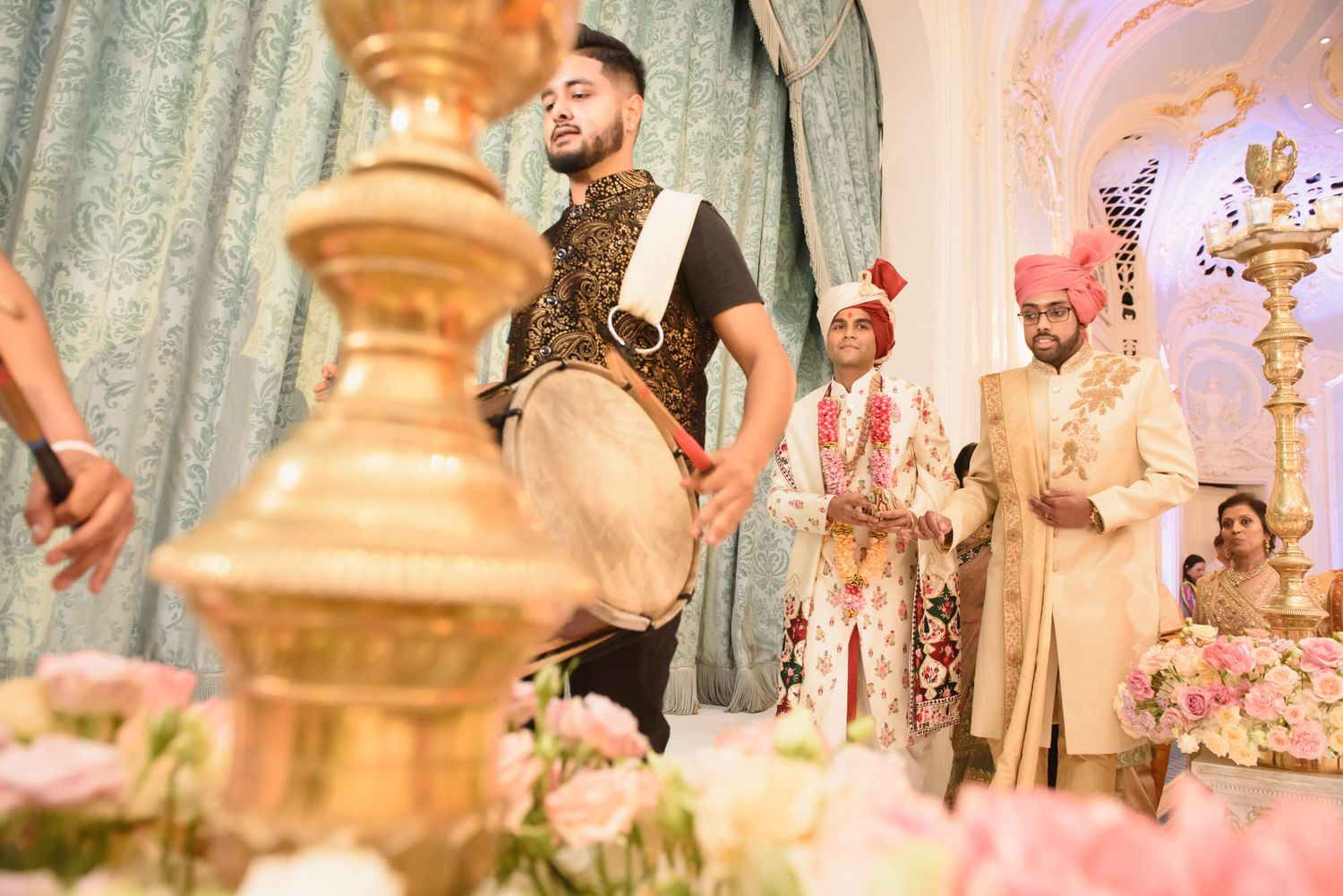 Dhol drummer performs at elegant Indian wedding ceremony with groom and guests at decorated mandap.